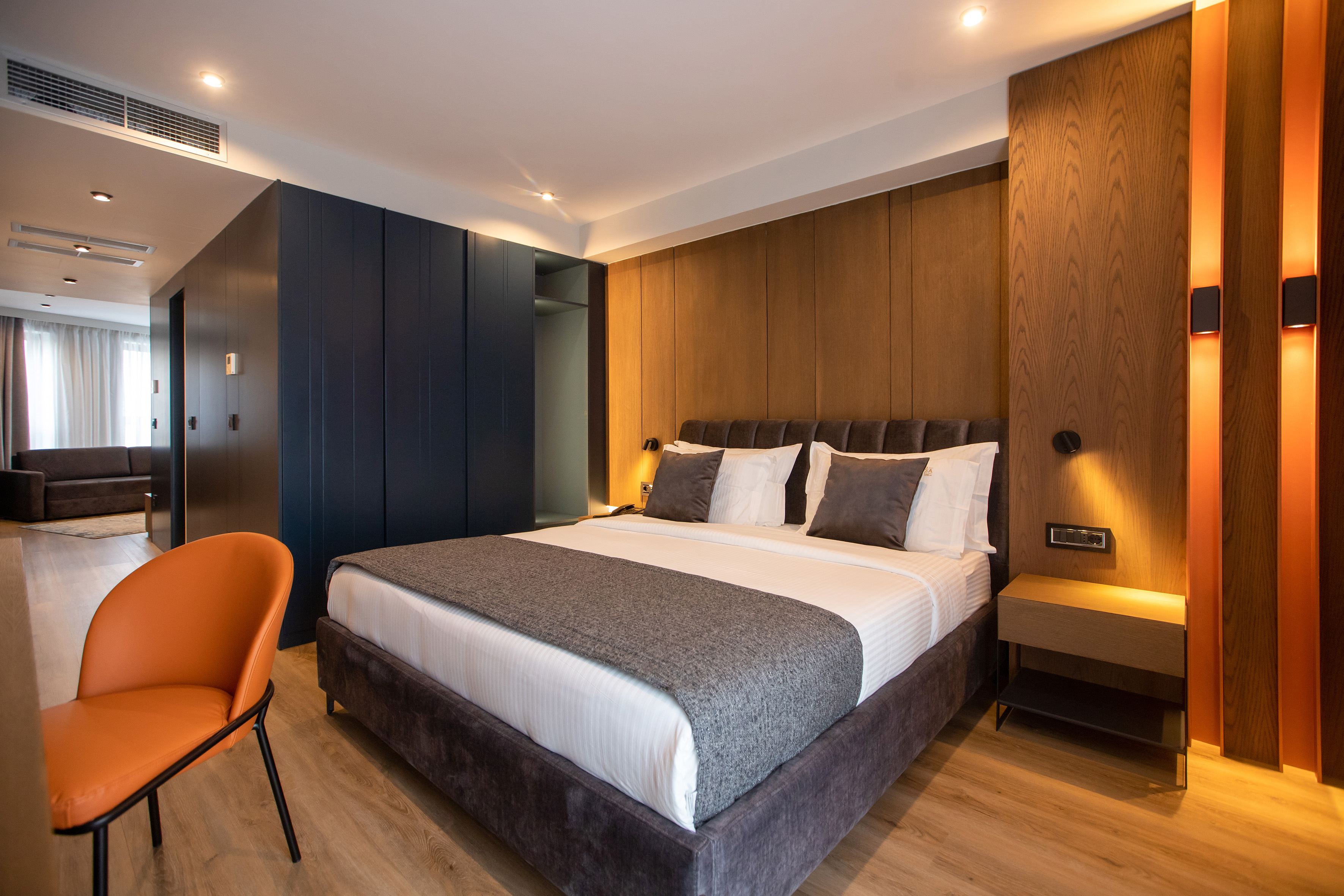 Modern hotel bedroom with large bed, wooden accent wall, and orange chair.