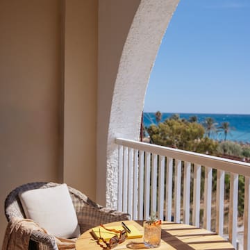 a table with glasses and a drink on a balcony overlooking the ocean