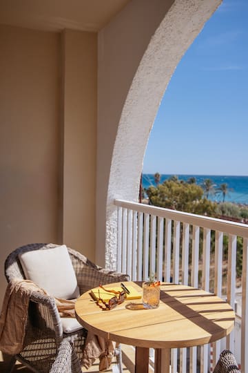 a table with glasses and a drink on a balcony overlooking the ocean