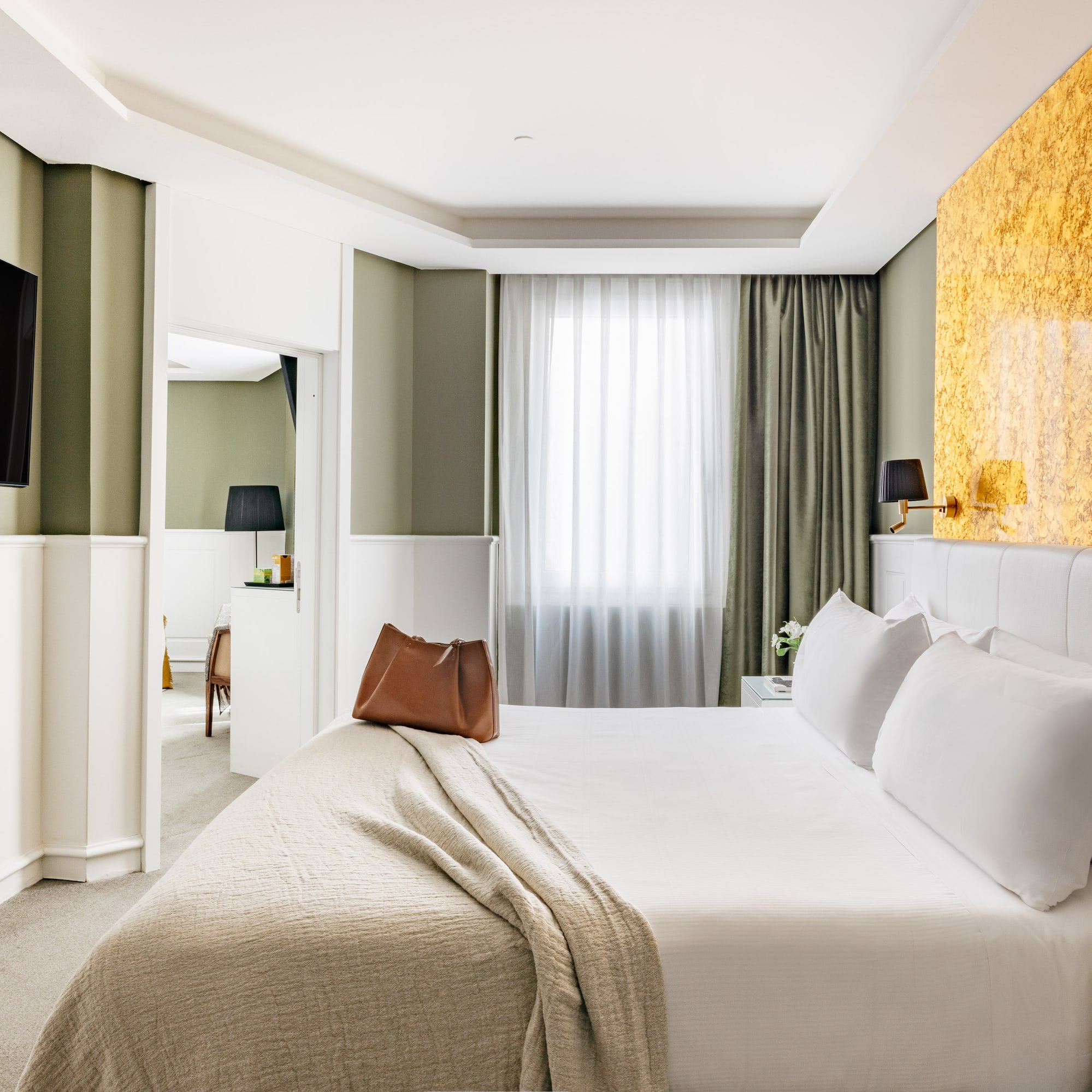 Habitación de hotel moderna con cama king, paredes verdes y detalles dorados.