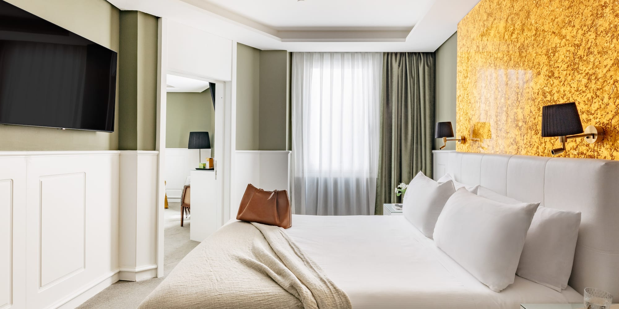 Habitación de hotel moderna con cama king, paredes verdes y detalles dorados.