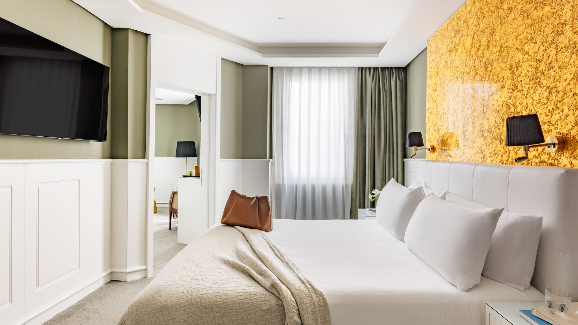 Habitación de hotel moderna con cama king, paredes verdes y detalles dorados.