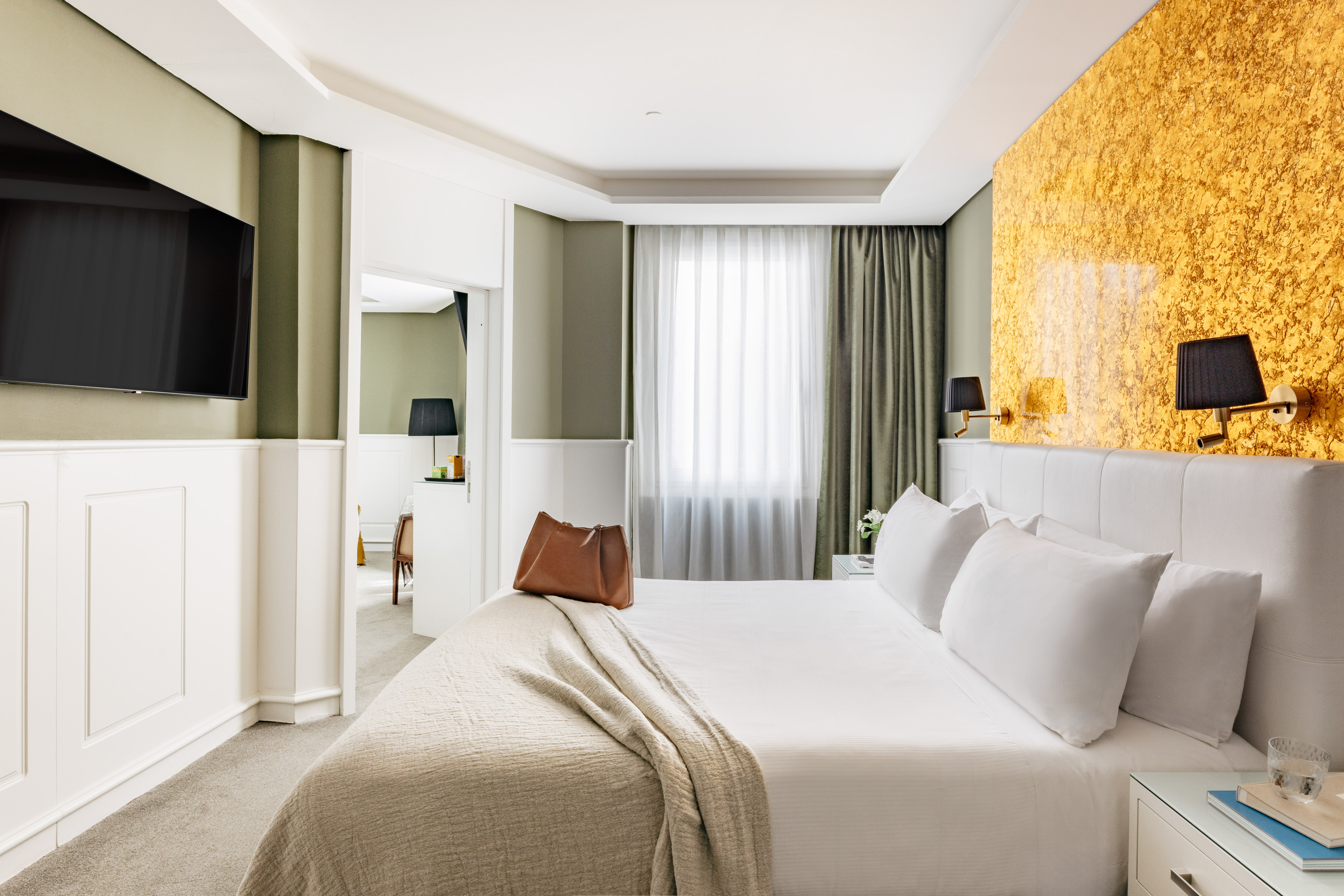 Habitación de hotel moderna con cama king, paredes verdes y detalles dorados.