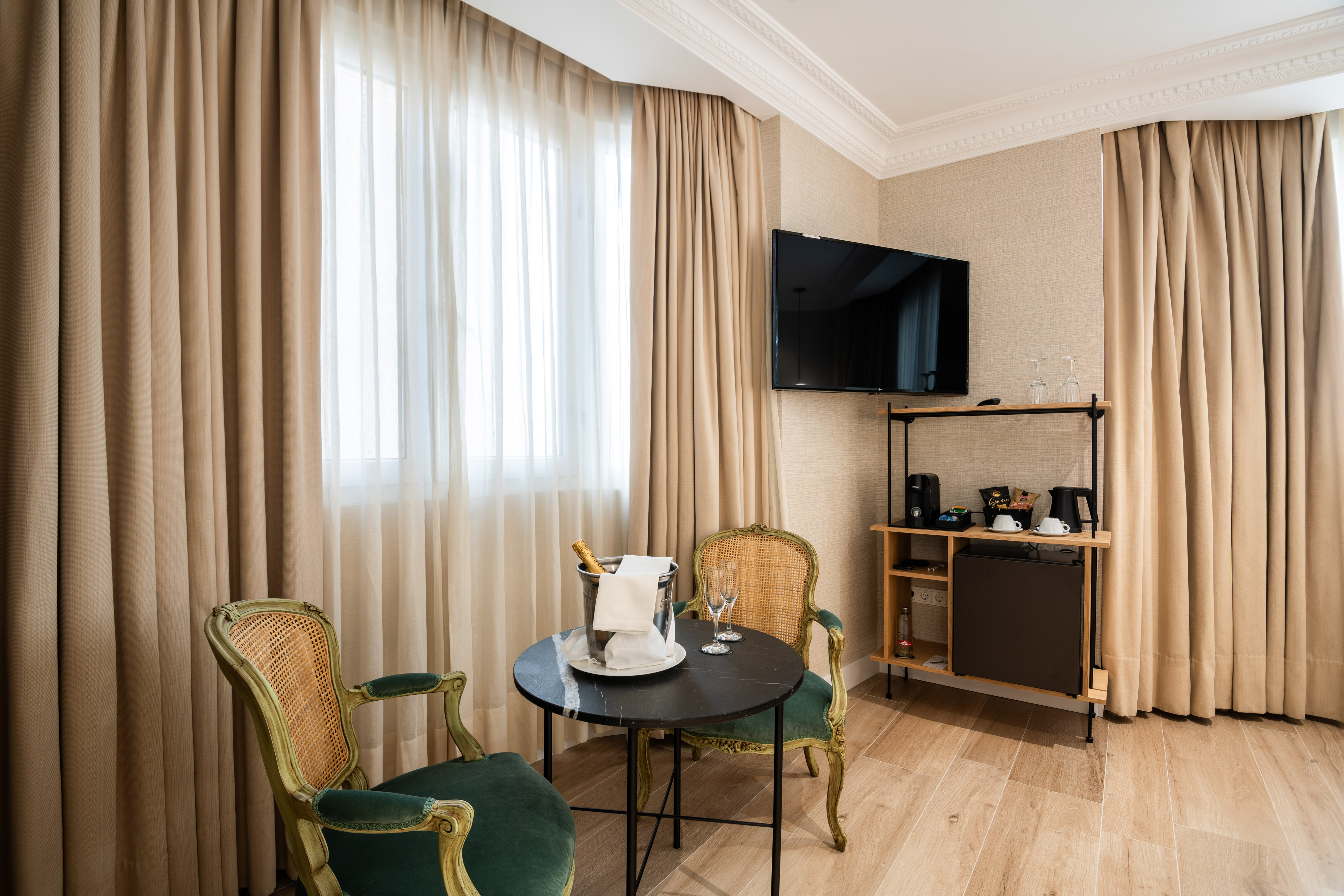 Hotel room with elegant chairs, champagne, minibar, and wall-mounted TV.