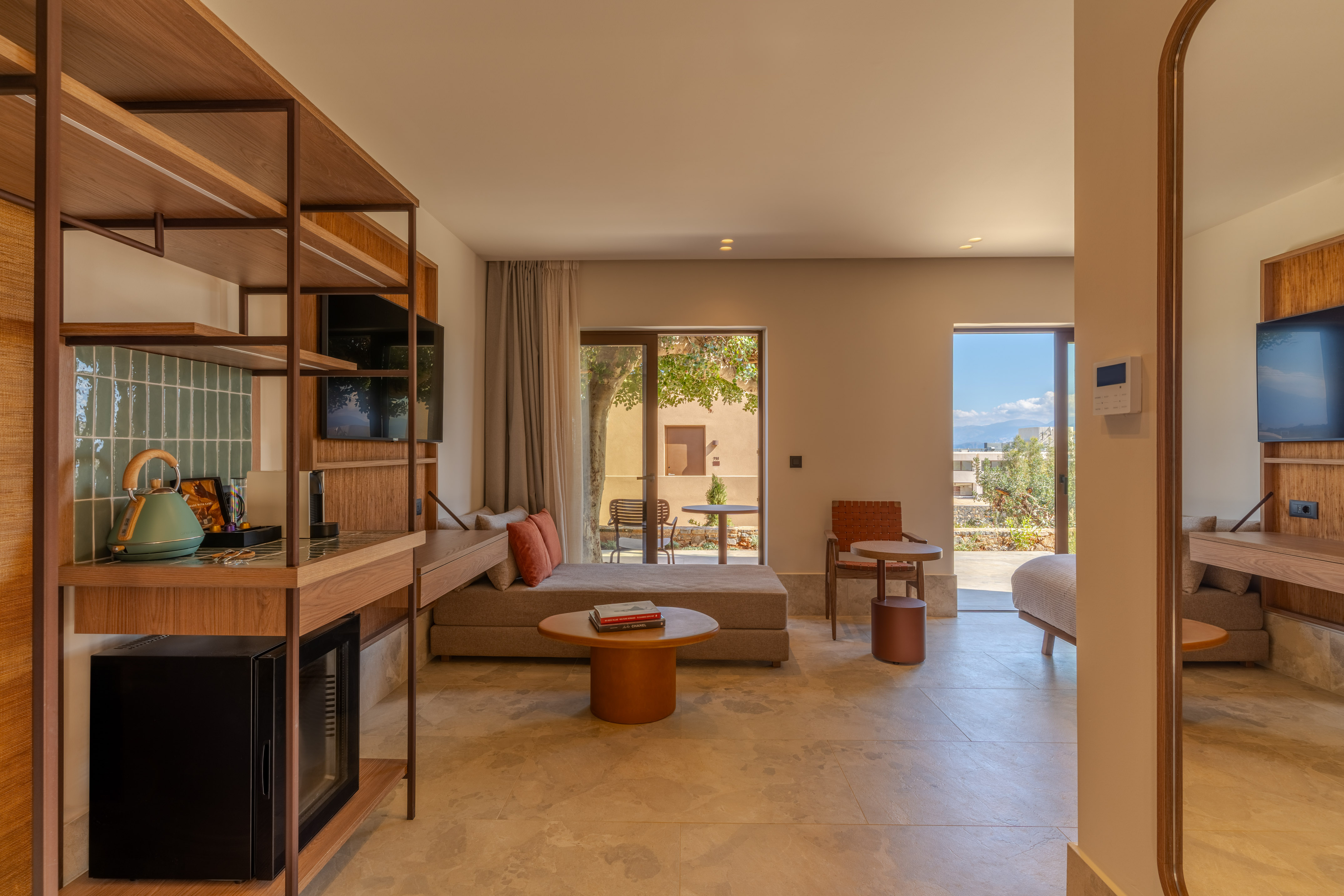 Modern hotel room with living area, minibar, TV, and outdoor terrace view.