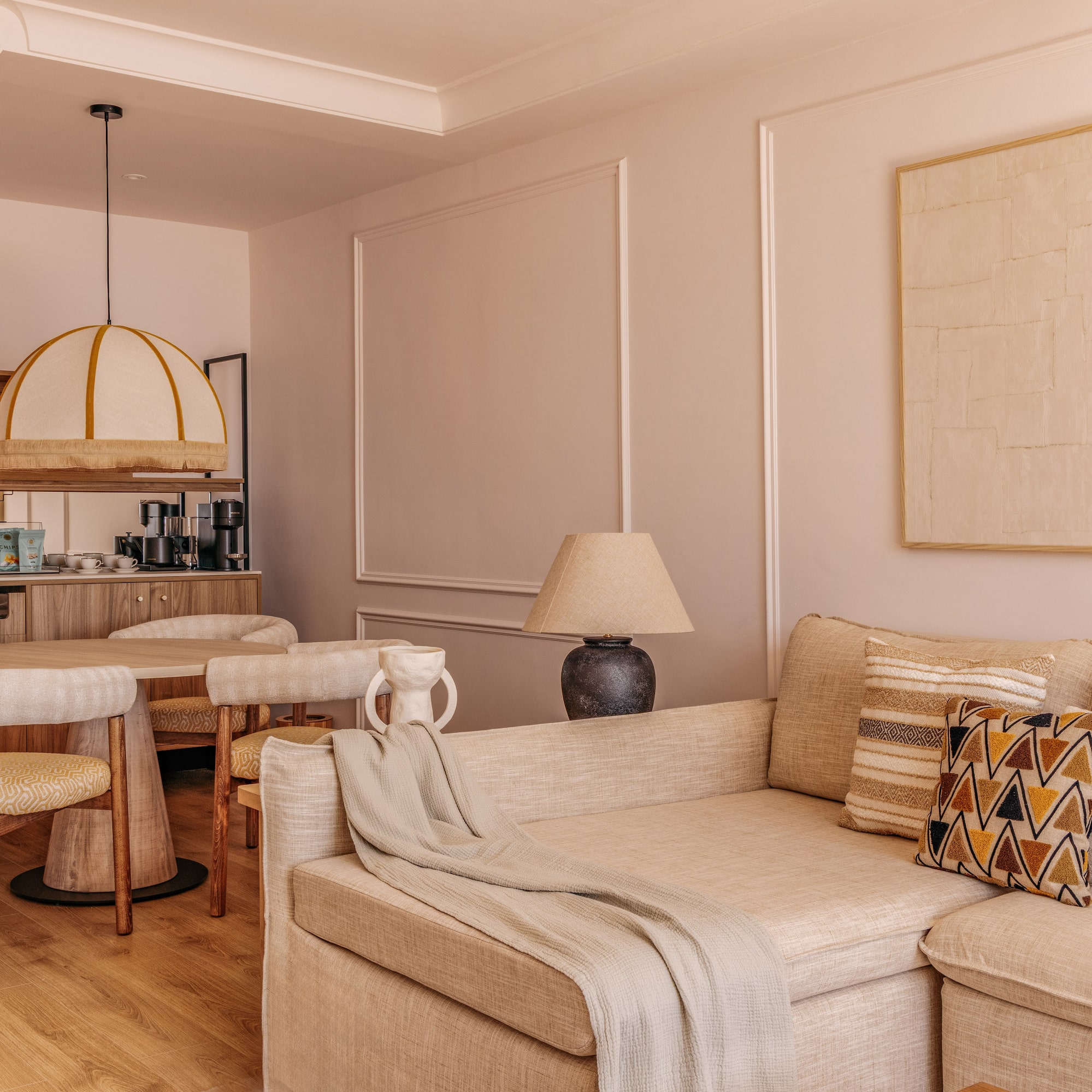 Cozy hotel suite living dining area with neutral sofa, round table, and mini-bar.