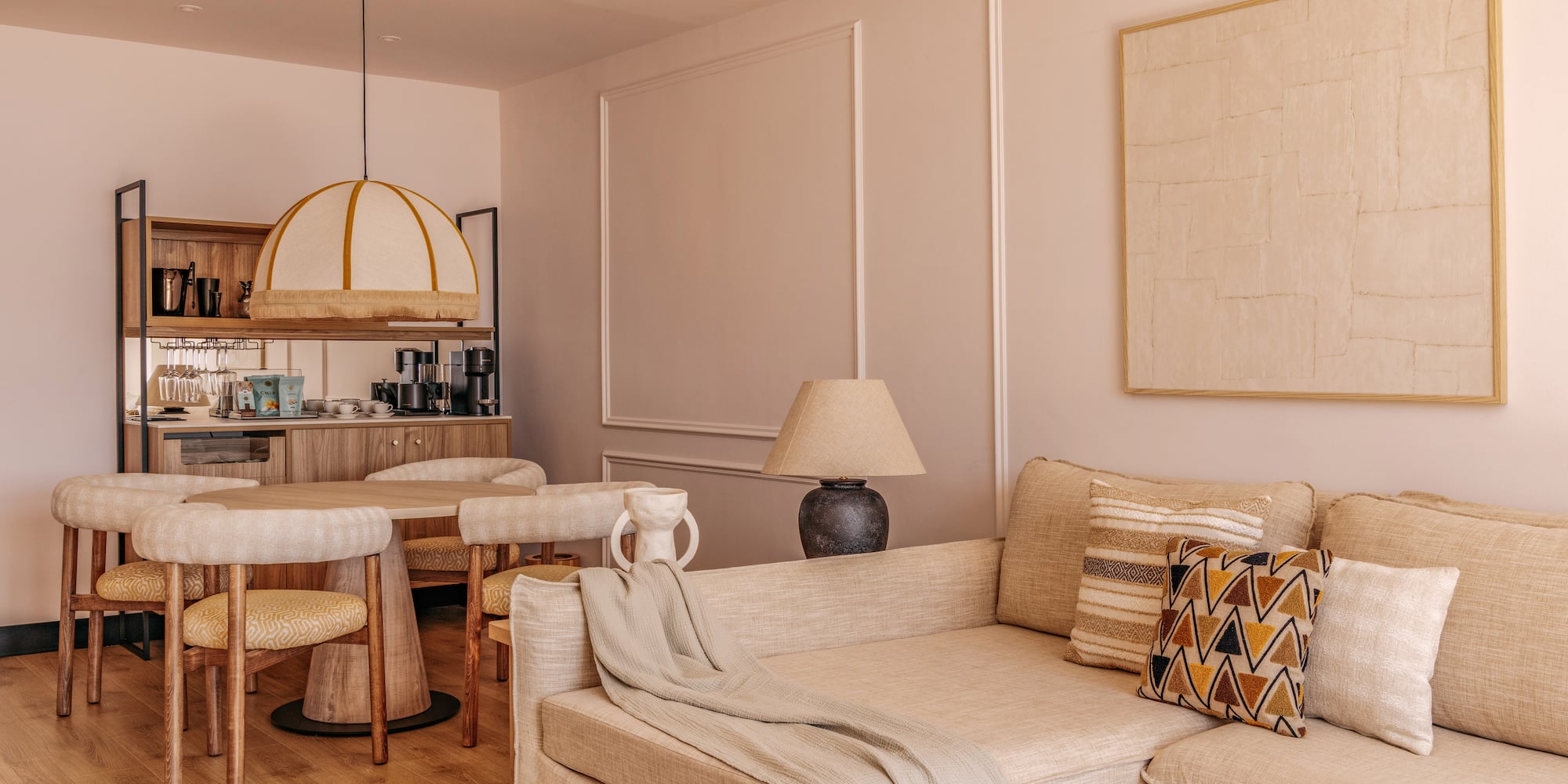 Cozy hotel suite living dining area with neutral sofa, round table, and mini-bar.