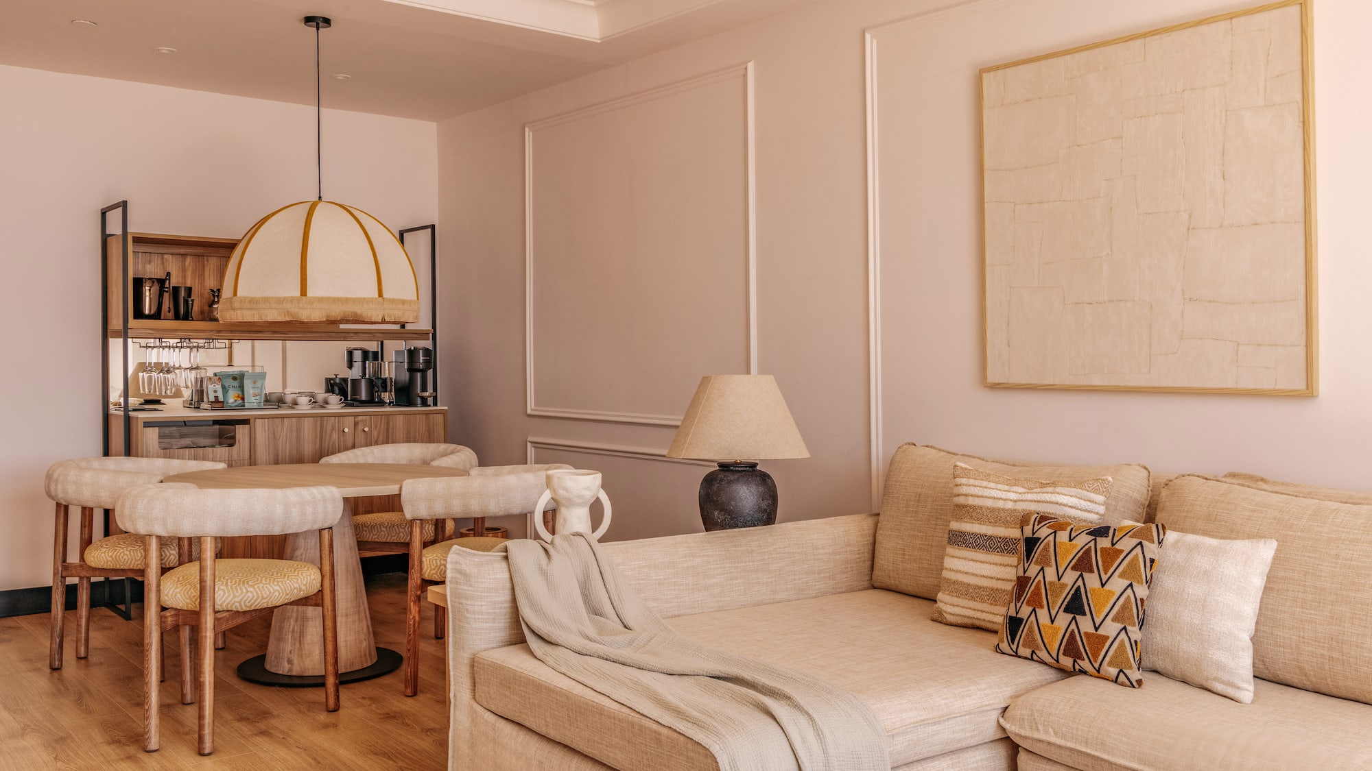 Cozy hotel suite living dining area with neutral sofa, round table, and mini-bar.