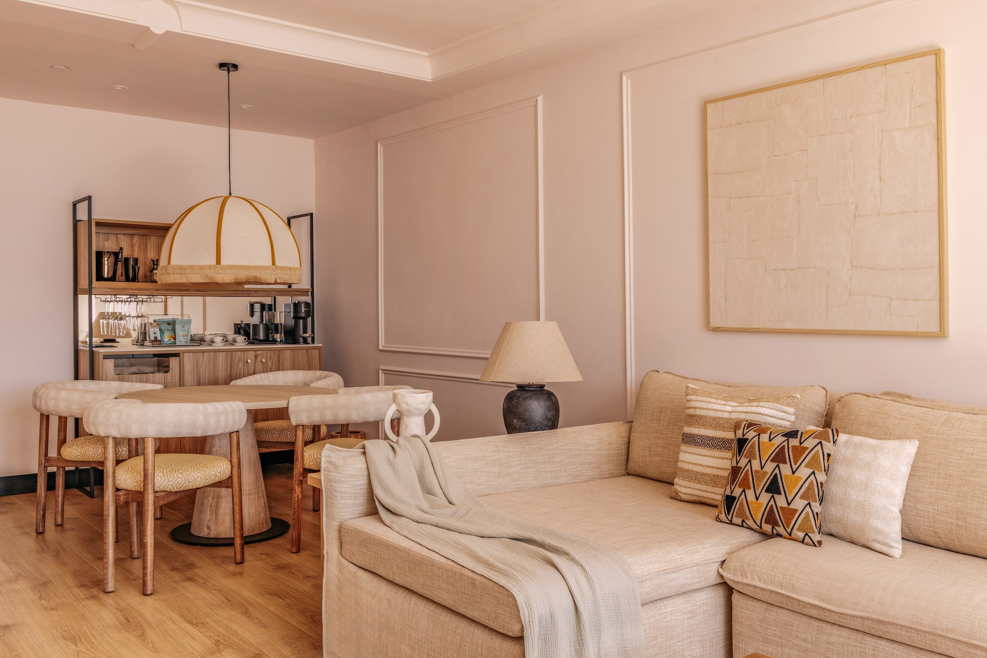 Cozy hotel suite living dining area with neutral sofa, round table, and mini-bar.