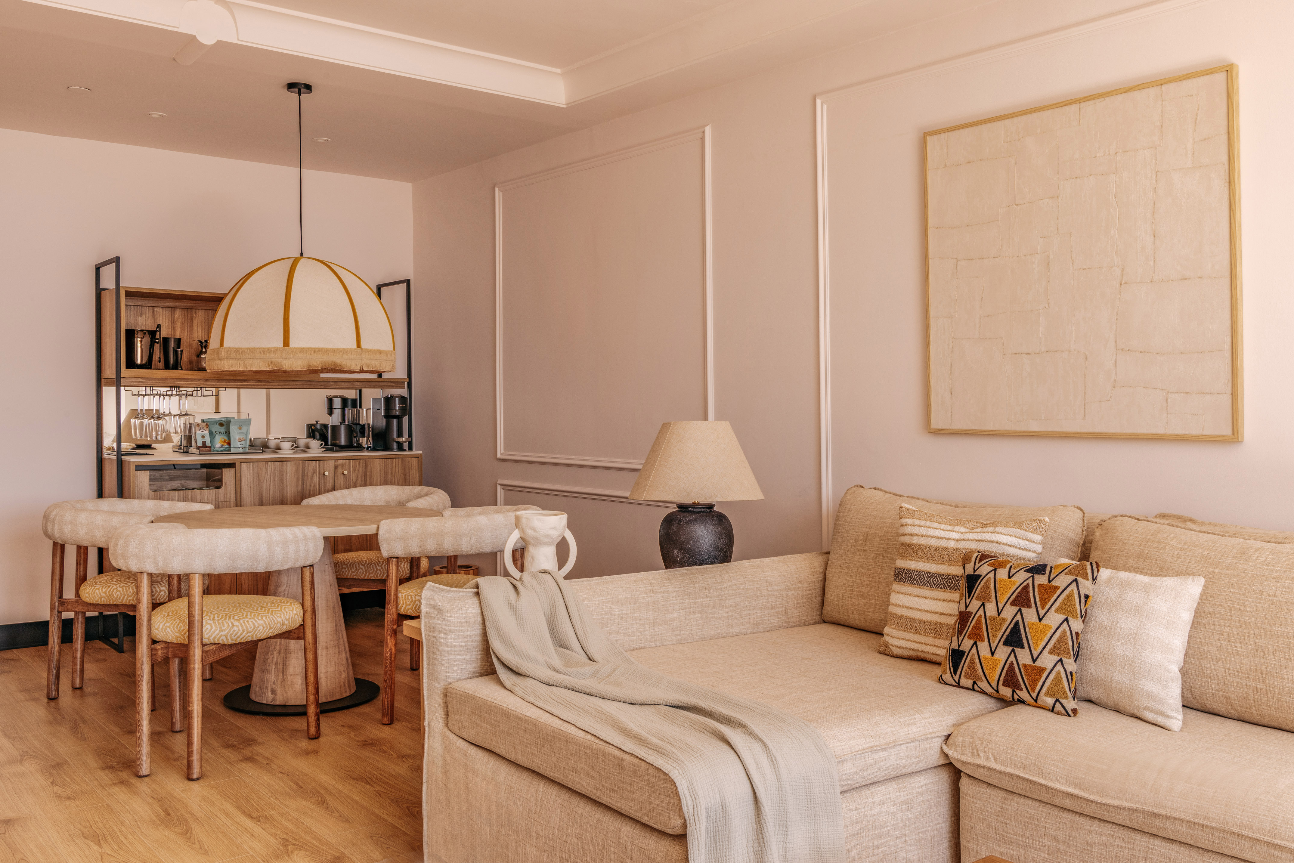 Cozy hotel suite living dining area with neutral sofa, round table, and mini-bar.
