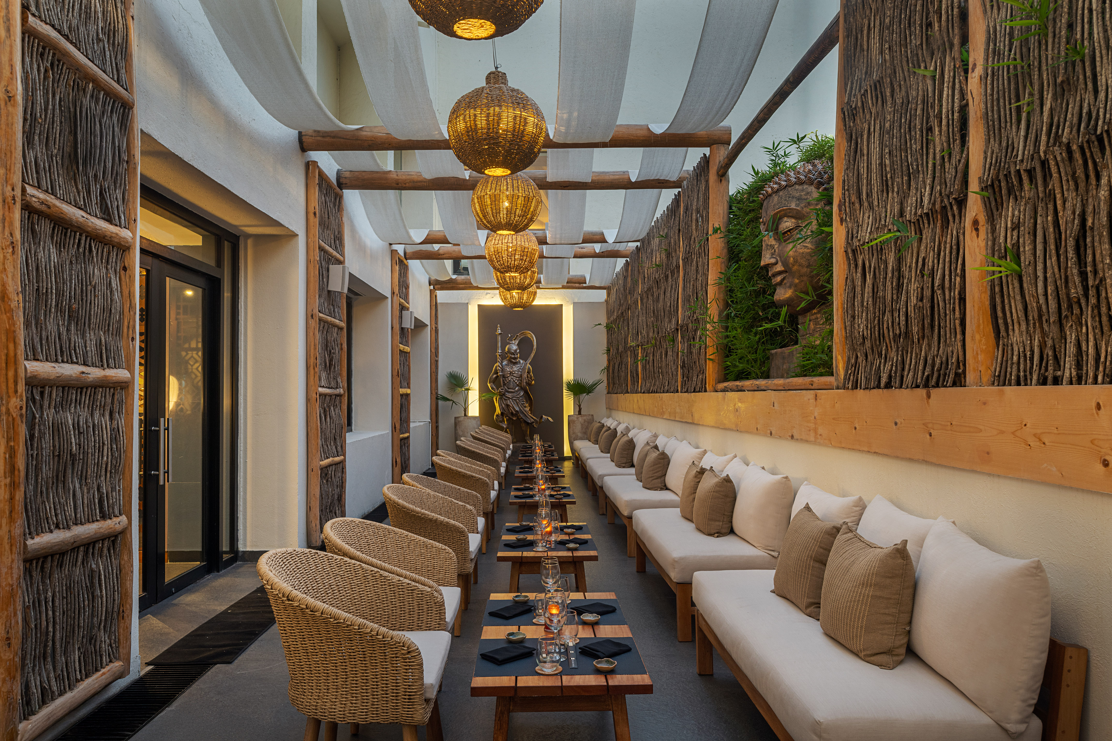 Zen outdoor dining patio with Buddha statue, wicker chairs, and hanging lanterns.