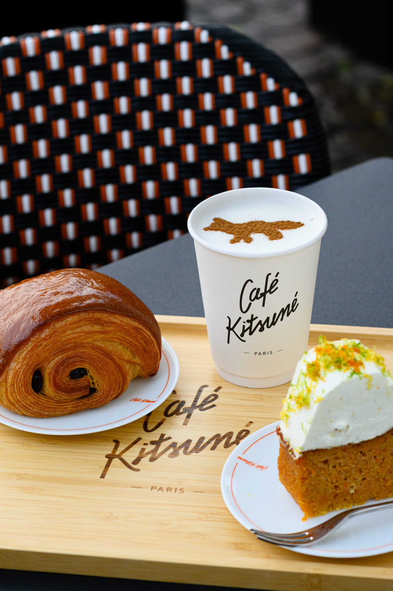 Café Kitsuné latte with fox art, pain au chocolat, and carrot cake on a tray.