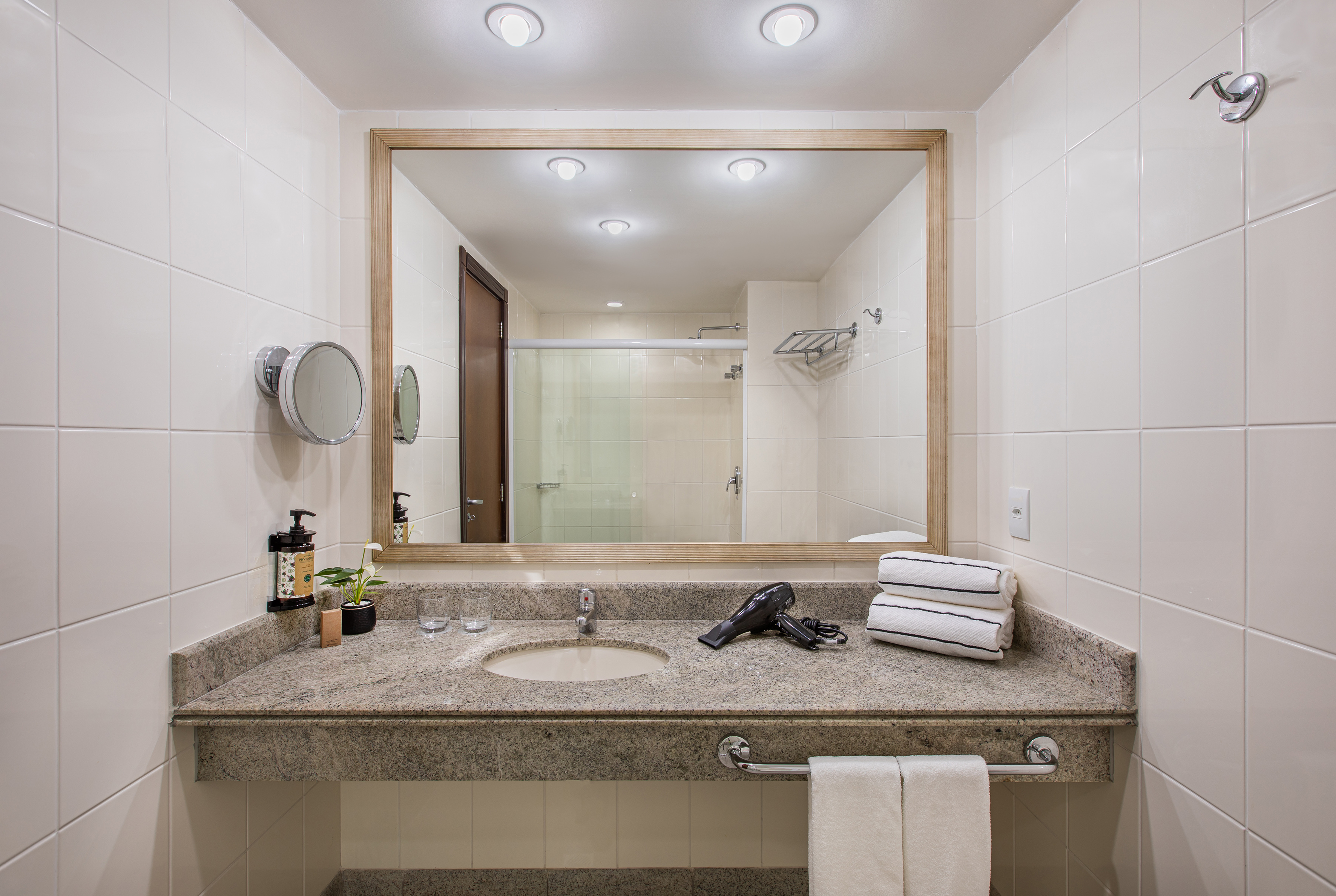 Modern hotel bathroom with granite vanity, large mirror, hairdryer, and towels.