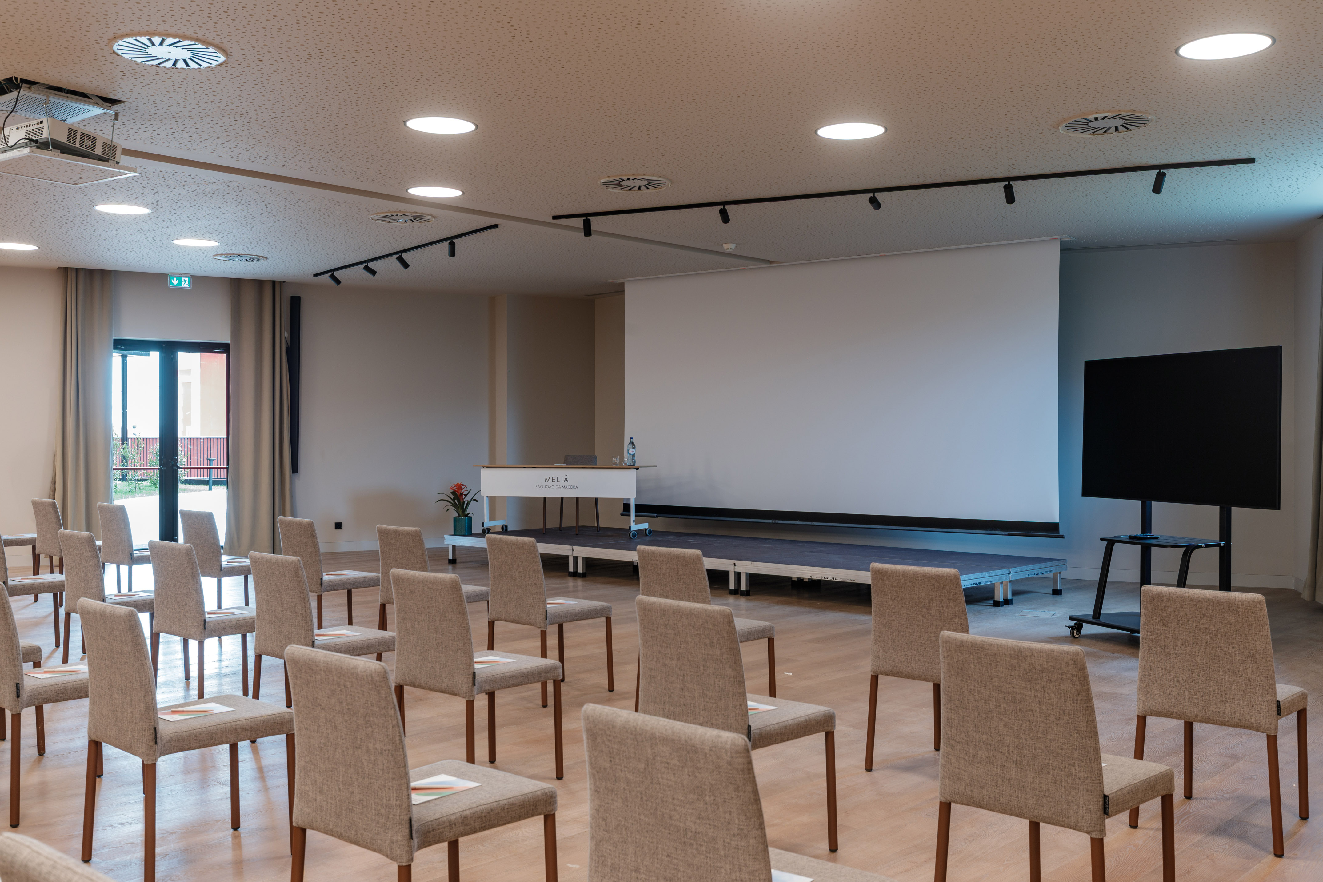 Meliá conference room with presentation screen, stage, upholstered chairs.