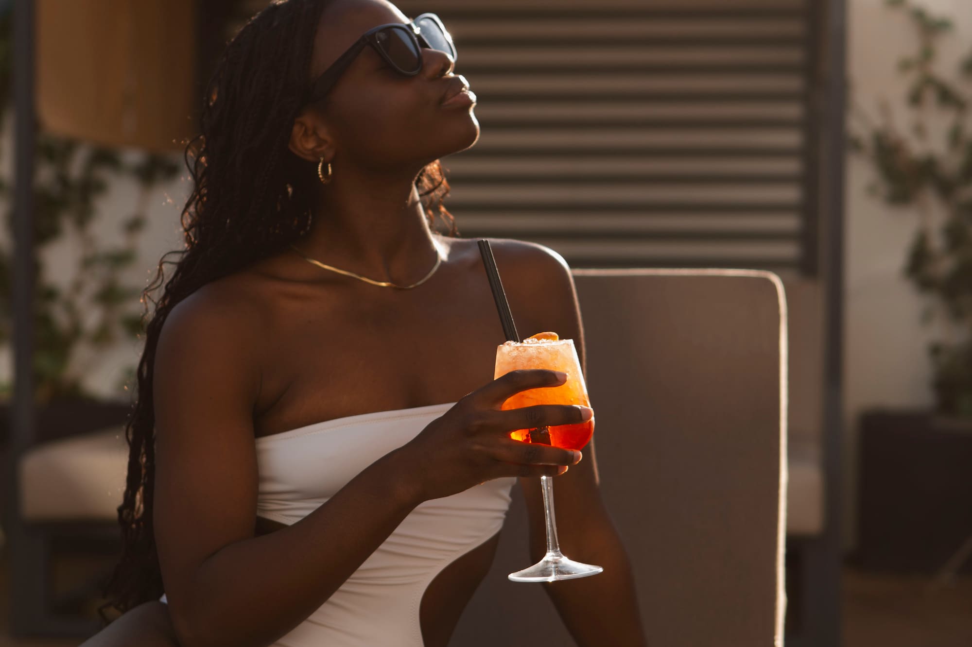 Black woman in white swimsuit, sunglasses, holding cocktail at Melia resort.