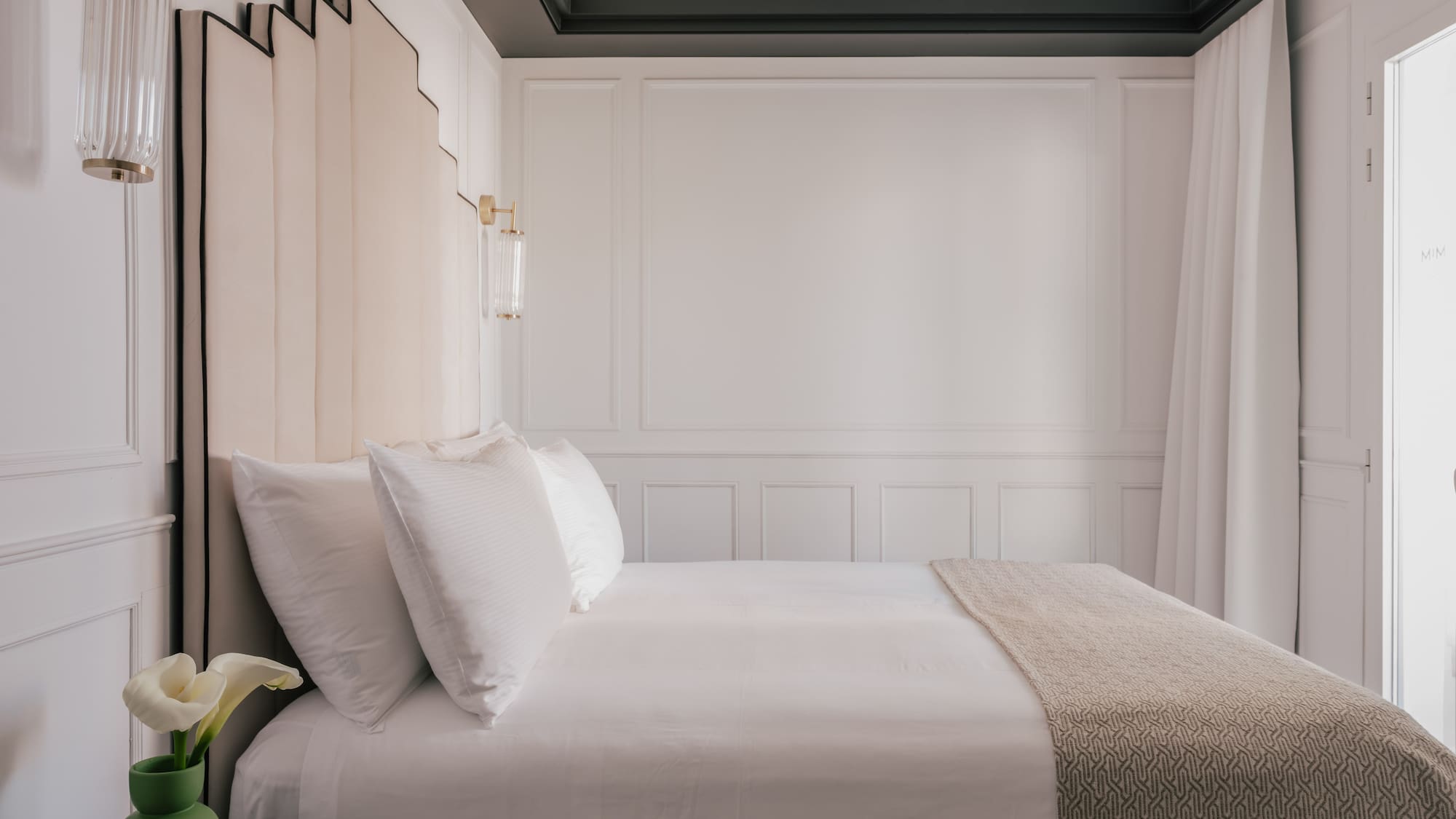 Luxury hotel bedroom with geometric headboard, white bed, and gold sconces.