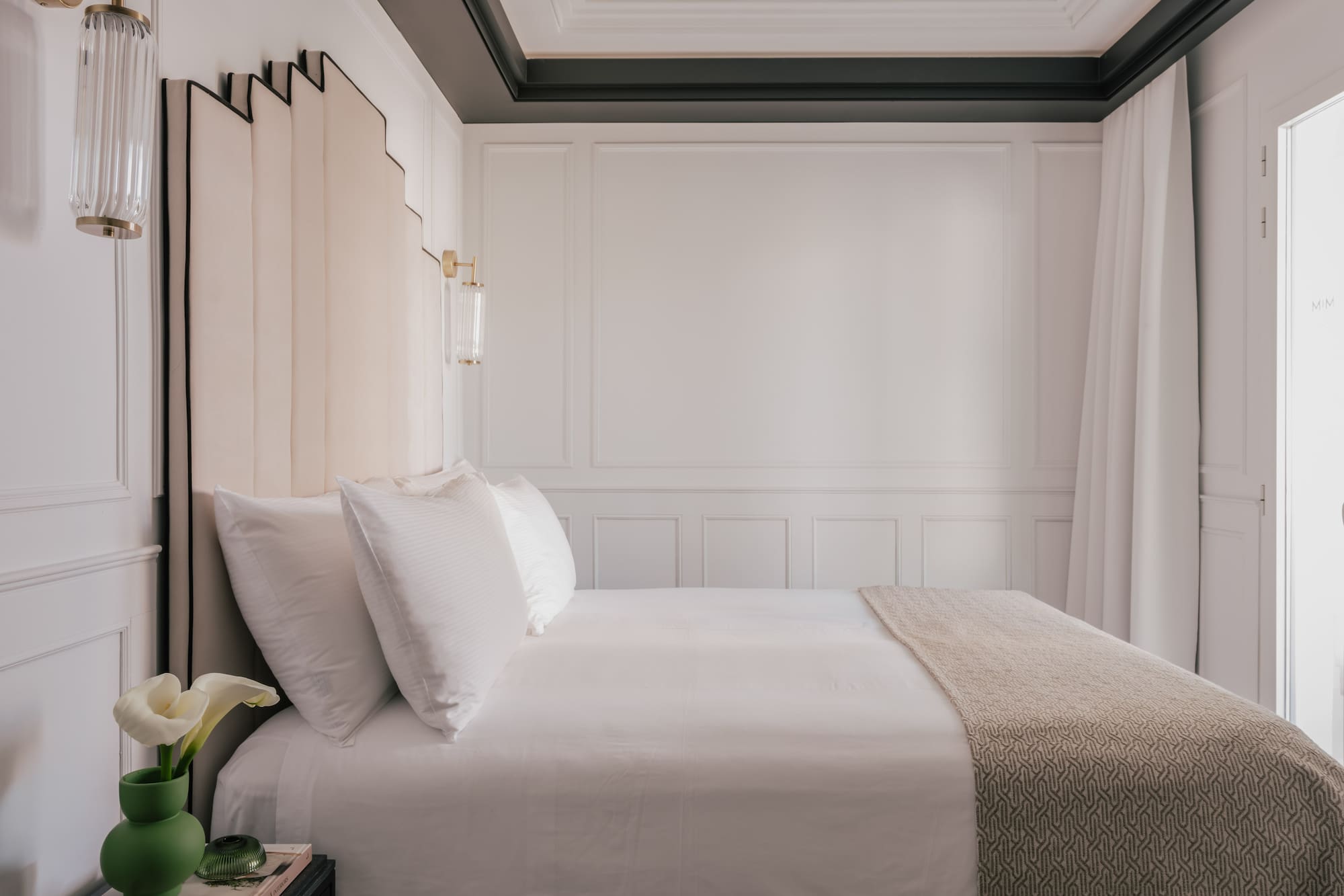 Luxury hotel bedroom with white bed, beige headboard, and gold wall sconces.