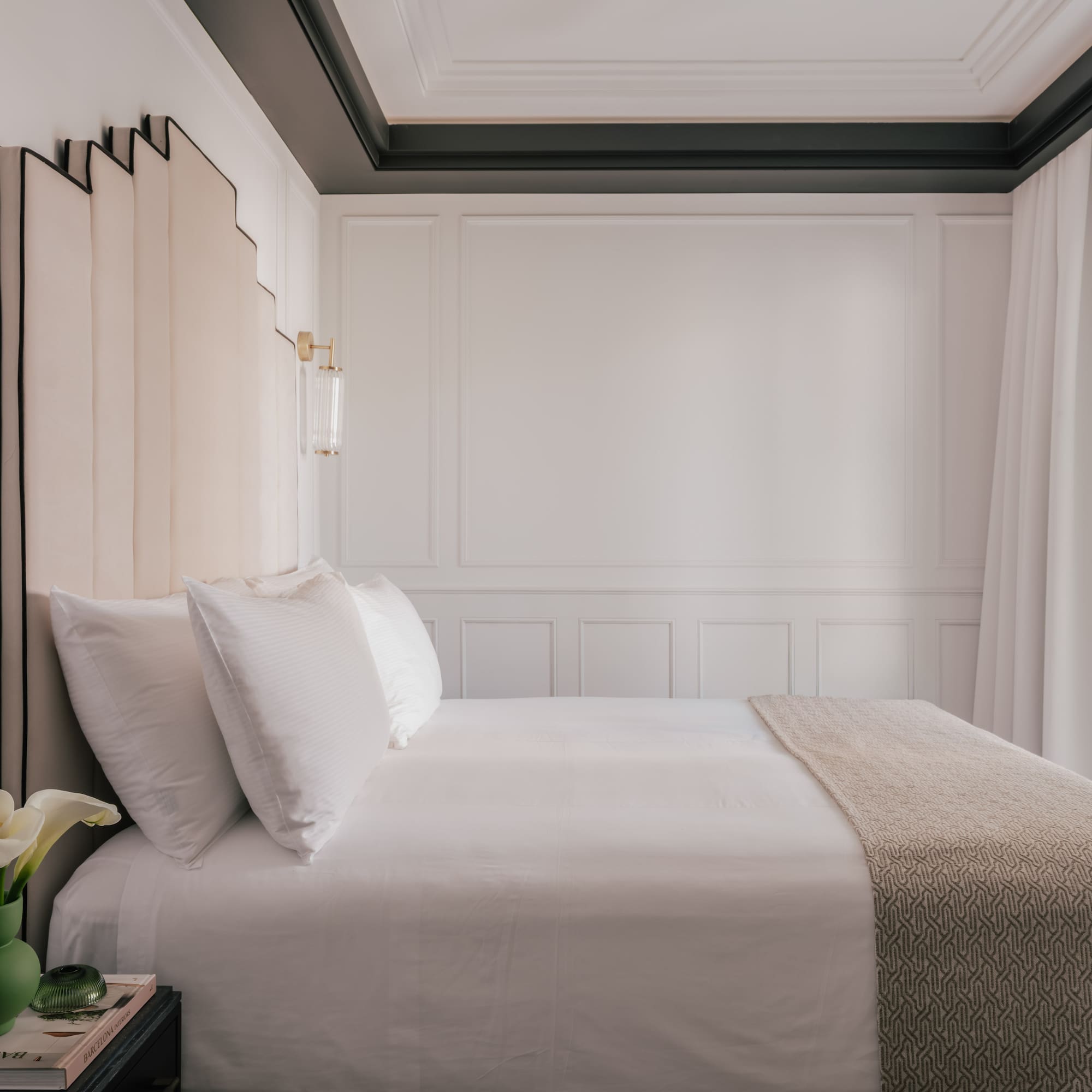 Luxury hotel bedroom with white bed, beige headboard, and gold wall sconces.