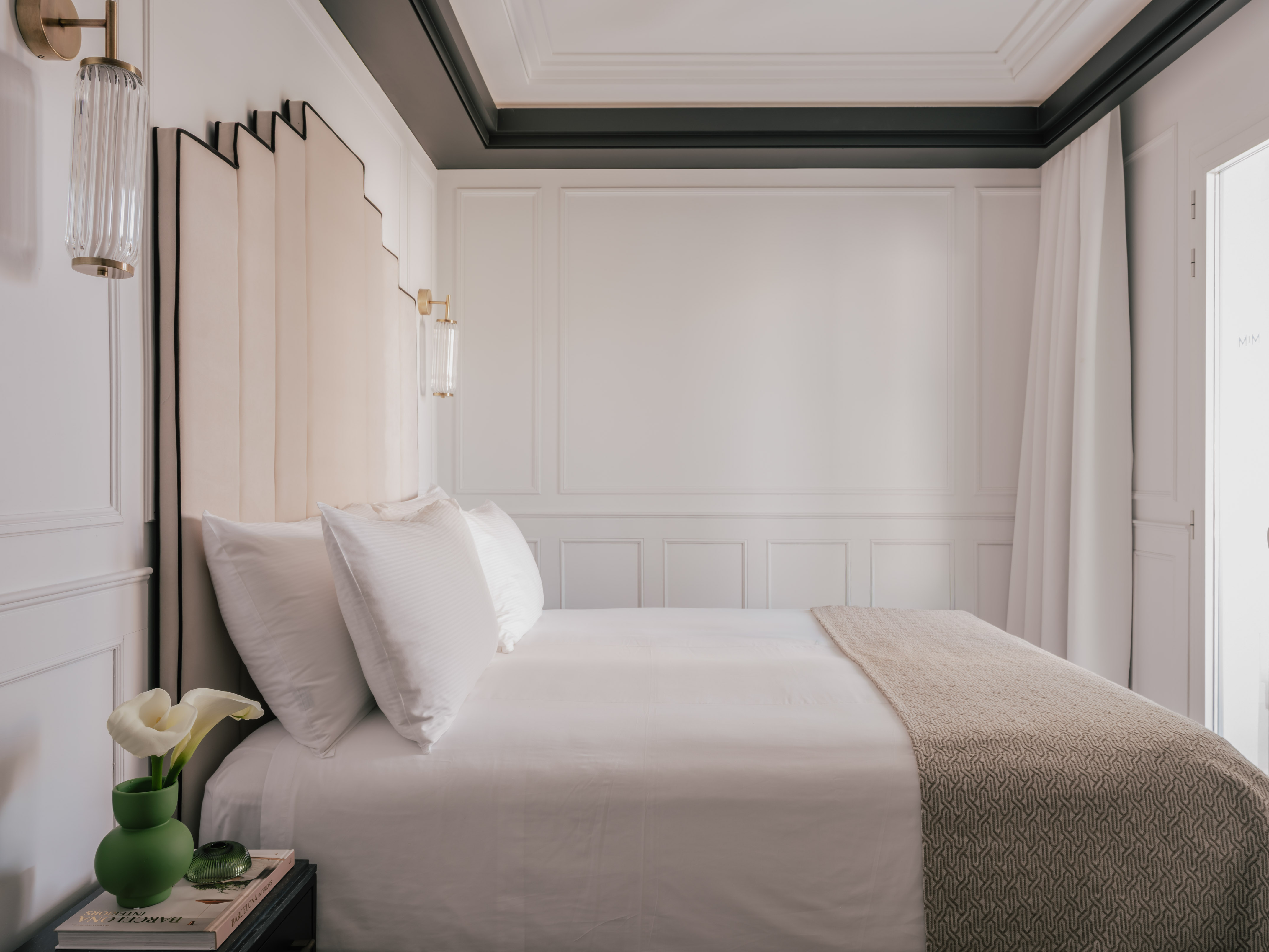 Luxury hotel bedroom with white bed, beige headboard, and gold wall sconces.