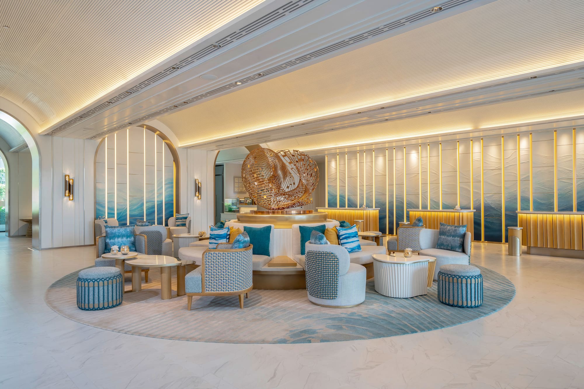 Modern hotel lobby with blue wave decor, circular lounge, golden sculpture.