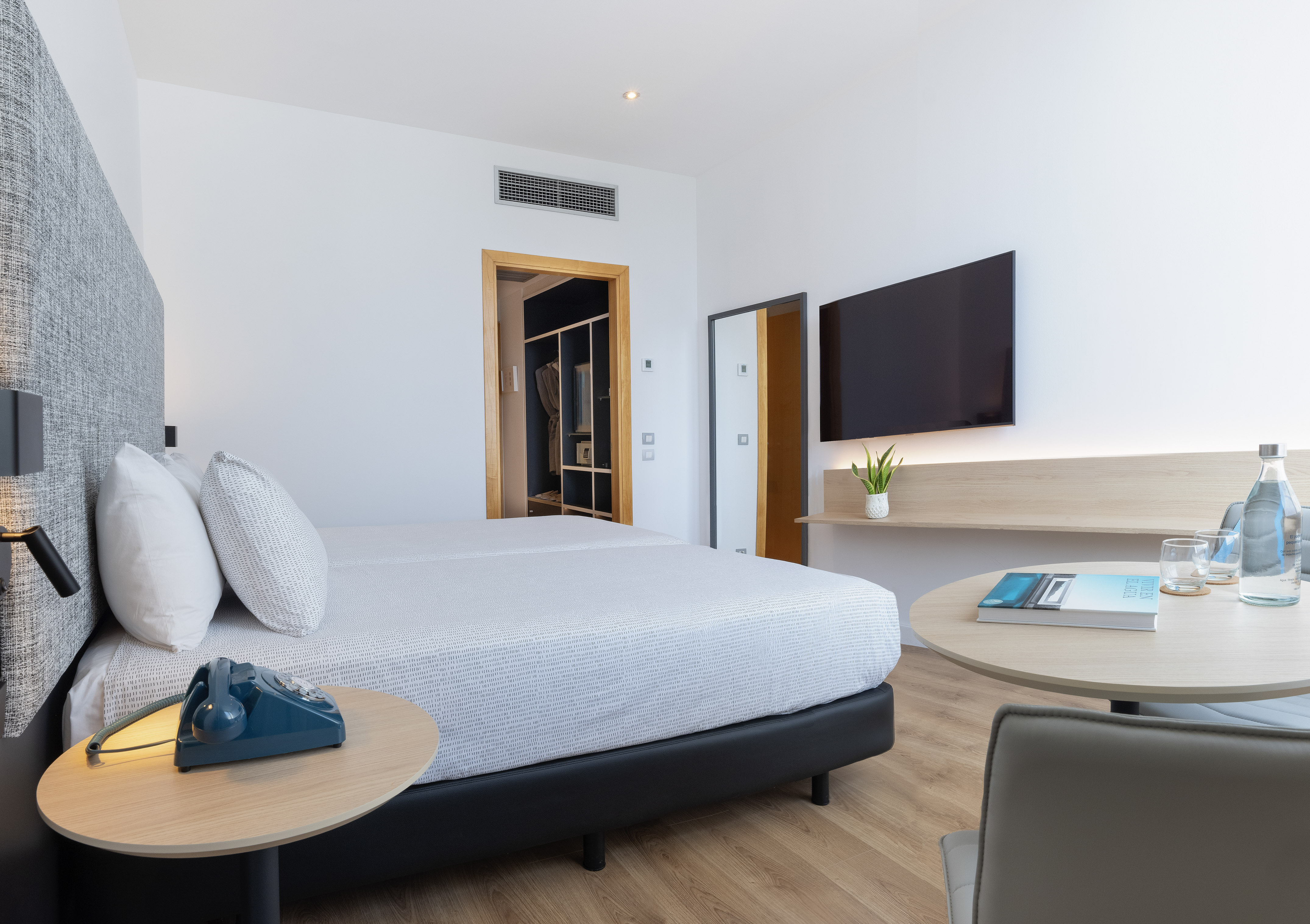 Modern hotel room with two beds, wall-mounted TV, and a vintage rotary phone.