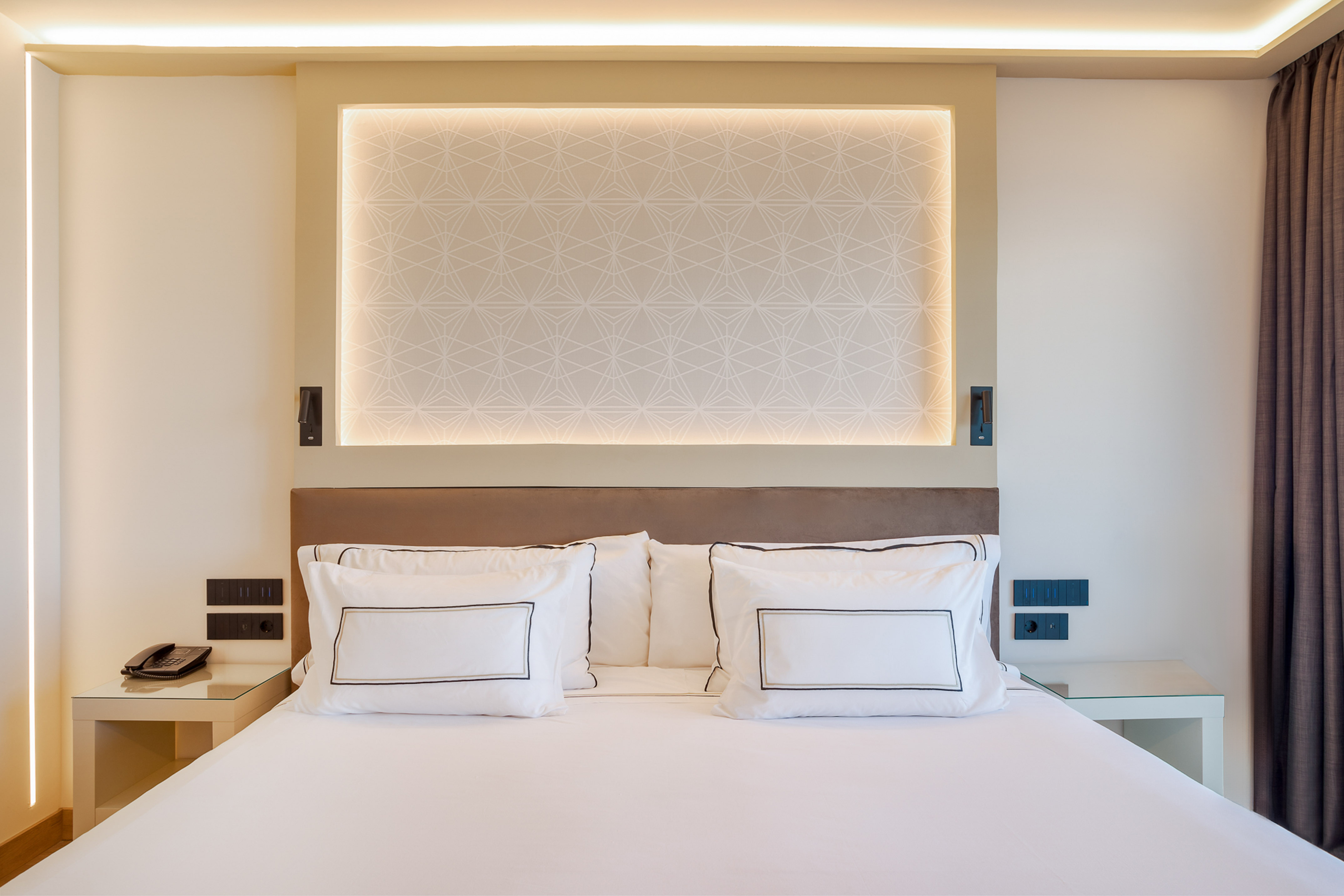 Modern hotel bedroom, white bed with geometric headboard and ambient lighting.