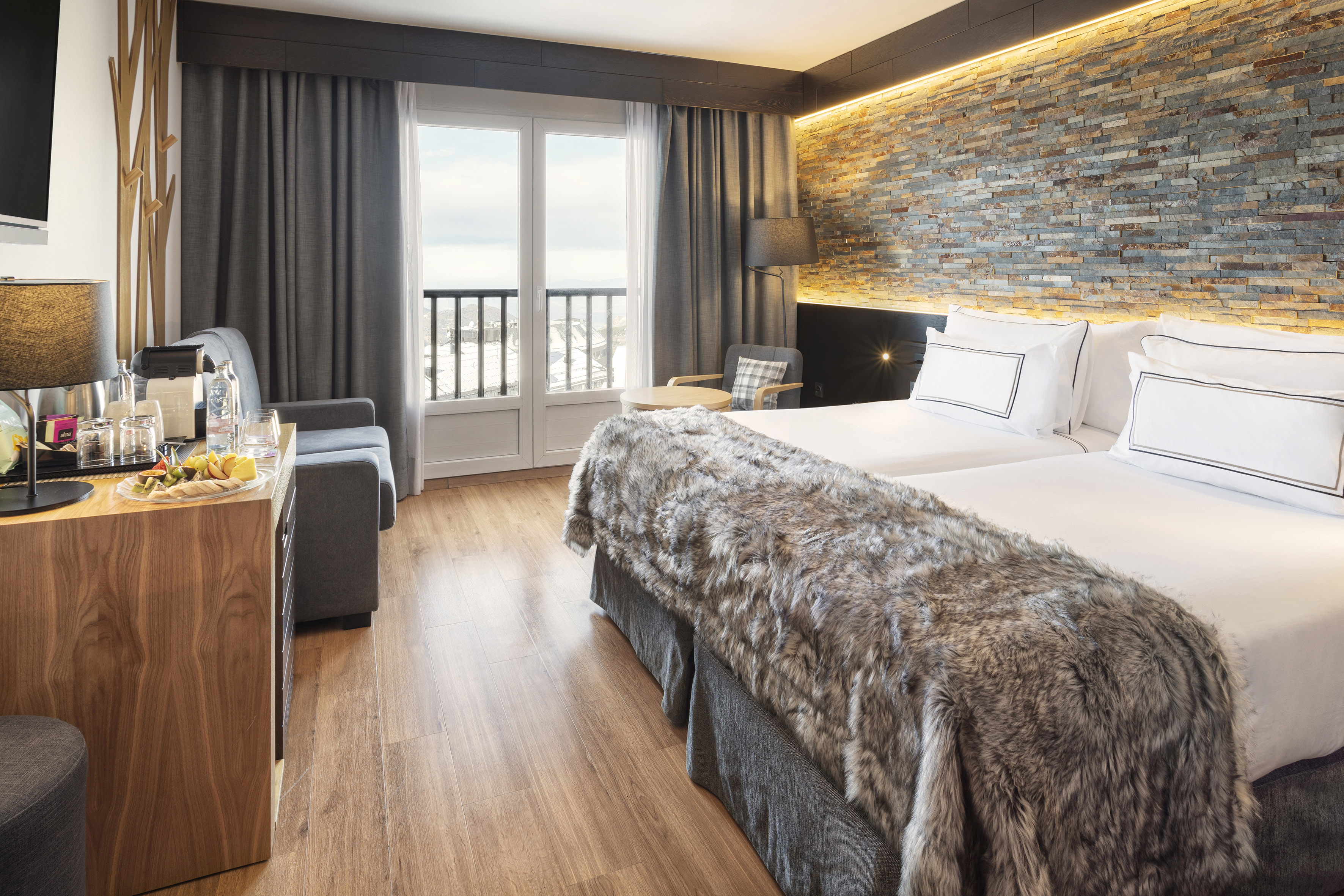 Luxury hotel room with twin beds, stone wall, fur throw, and balcony mountain view.