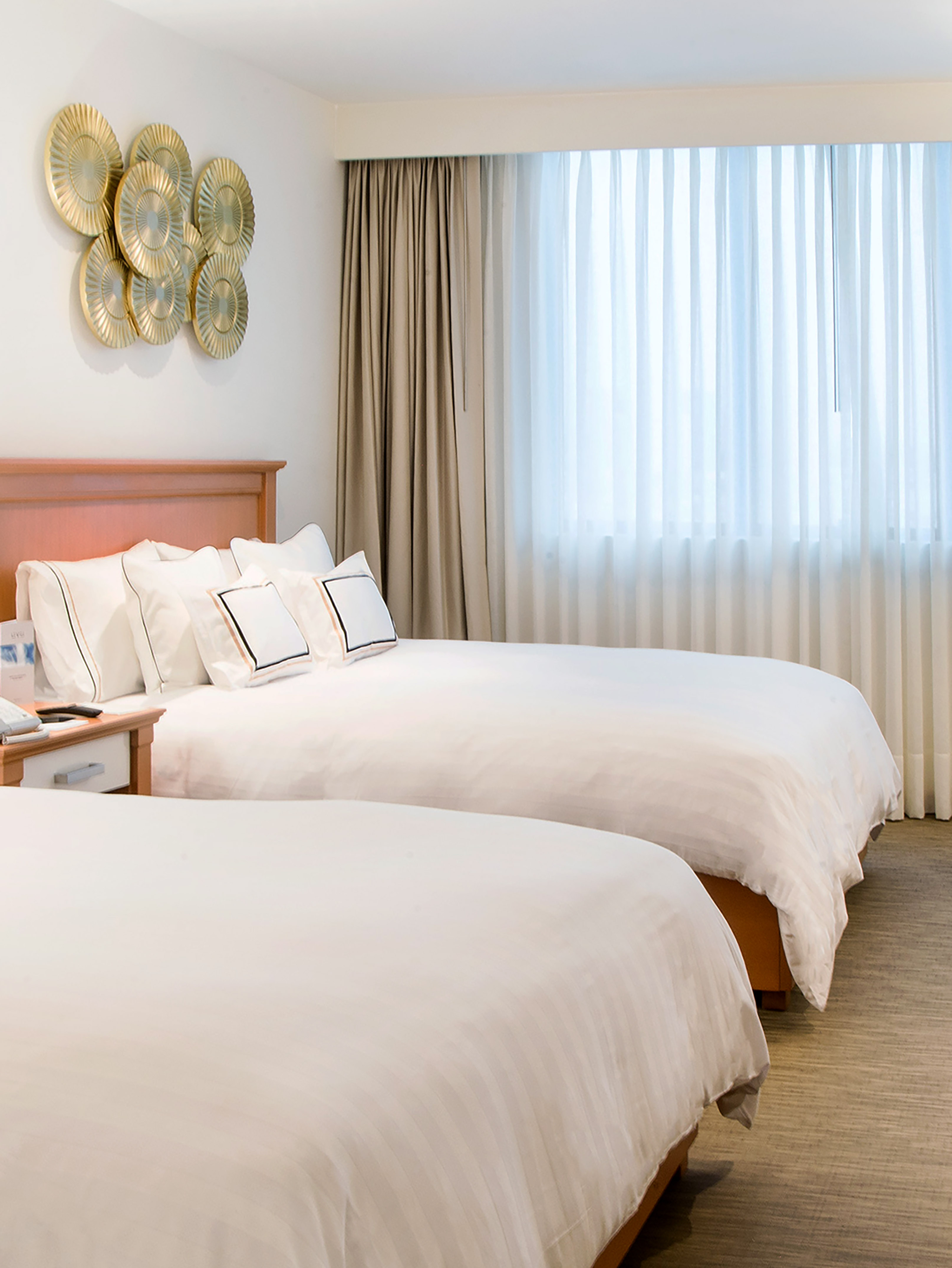 Hotel room with two twin beds, white bedding, golden round wall decor.