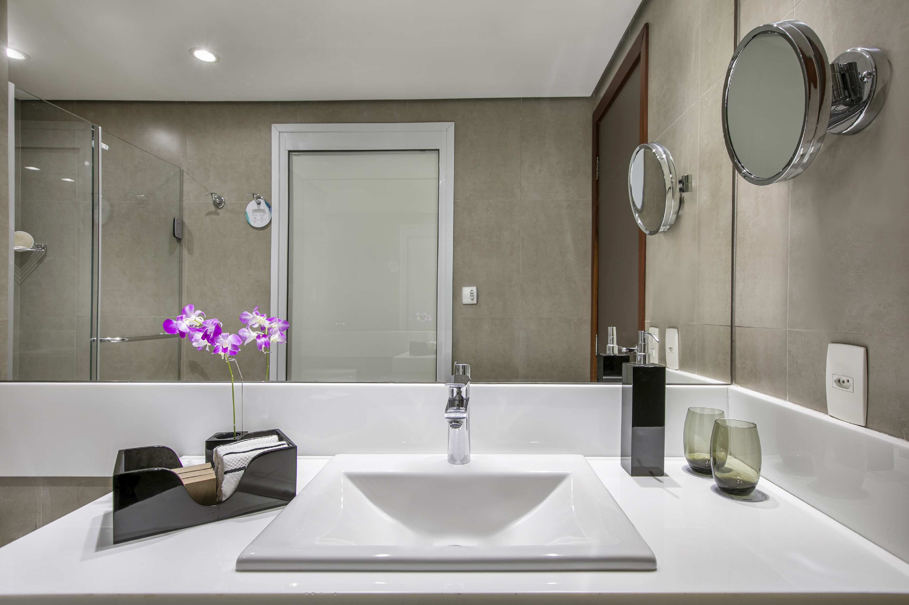 Hotel bathroom vanity with white sink, chrome faucet, mirror, and pink orchids.