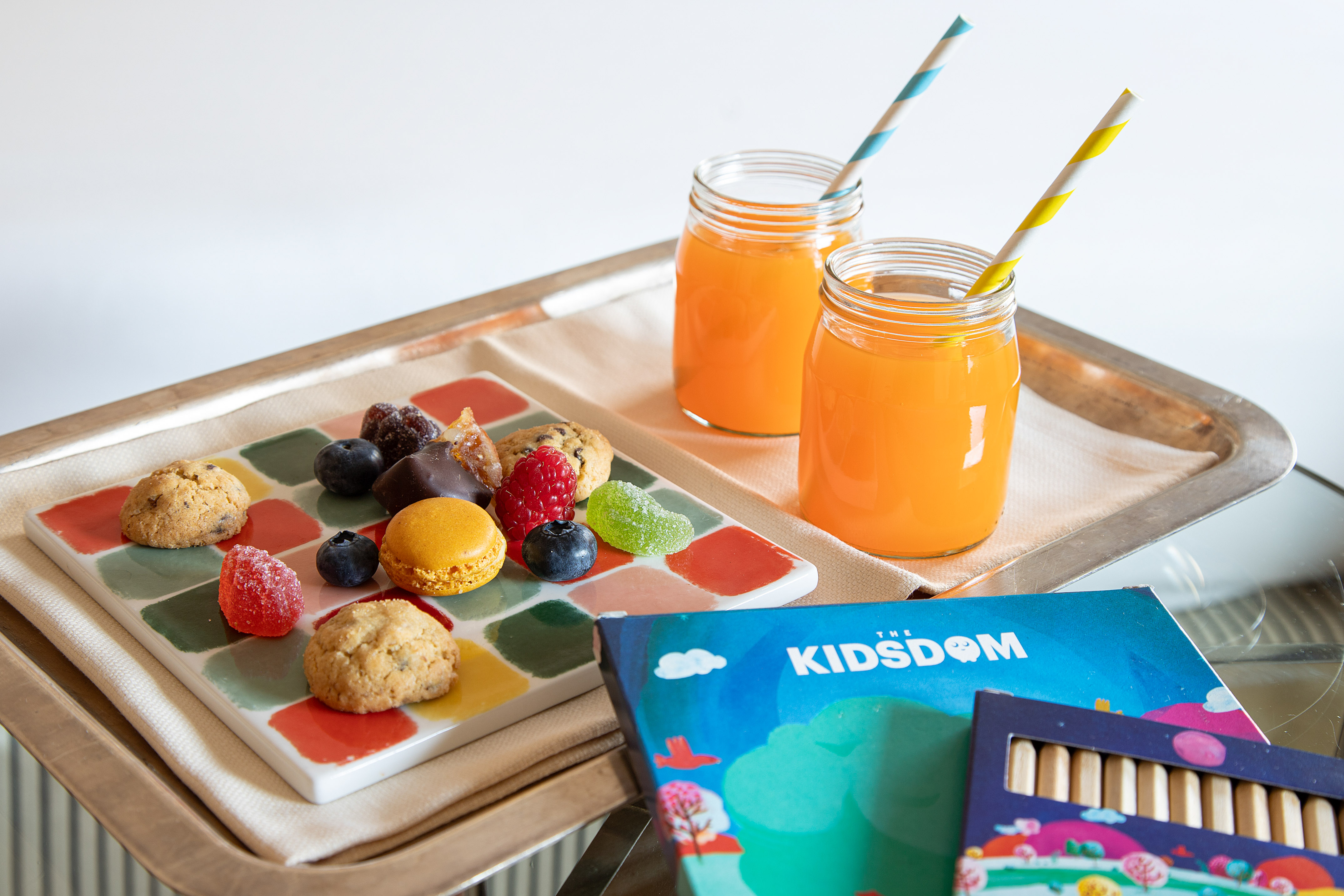 Kids' welcome tray: juice, cookies, macarons, berries, and activity book.