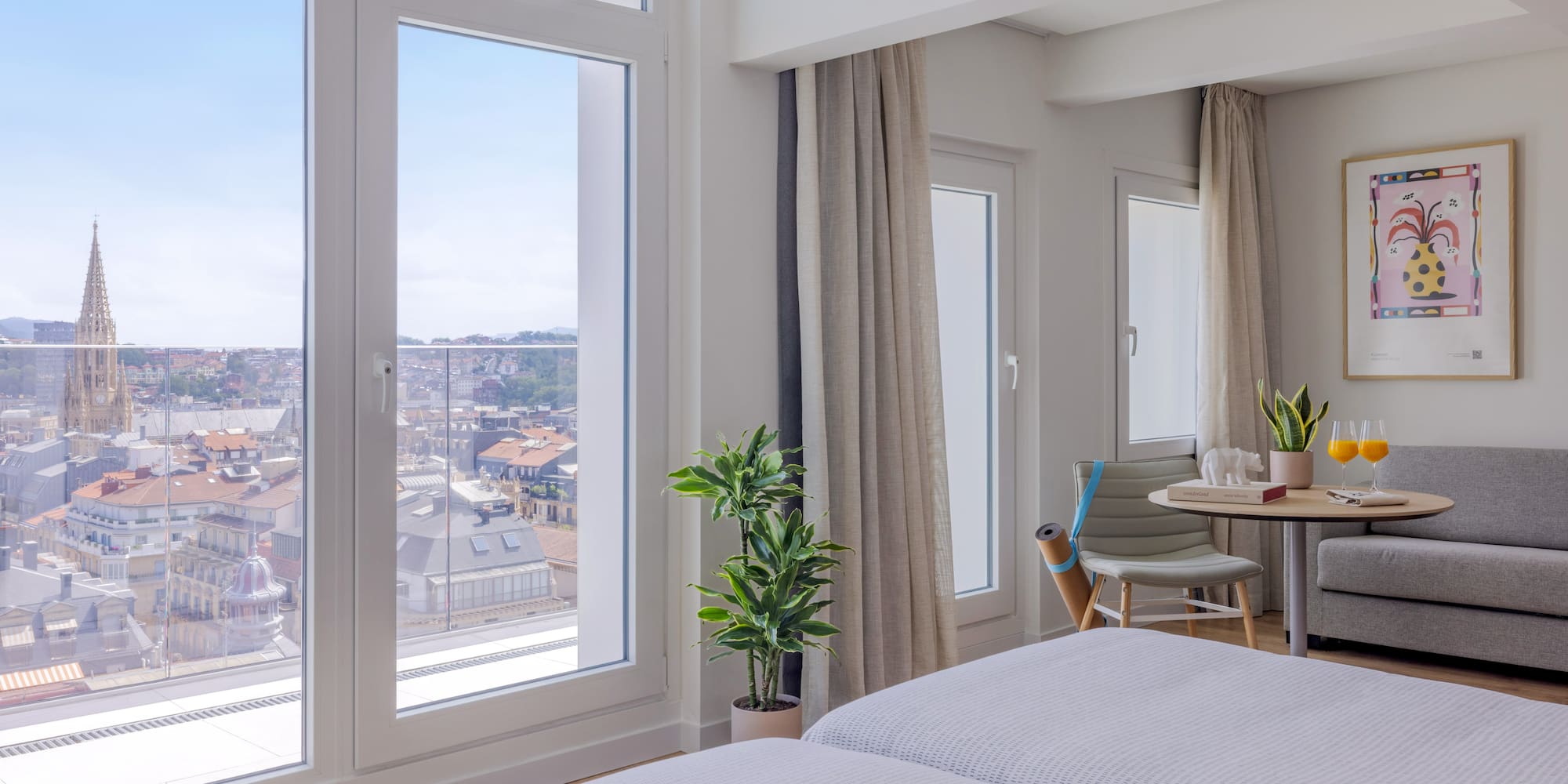 Habitación de hotel moderna con ventanales y vista urbana a la catedral.