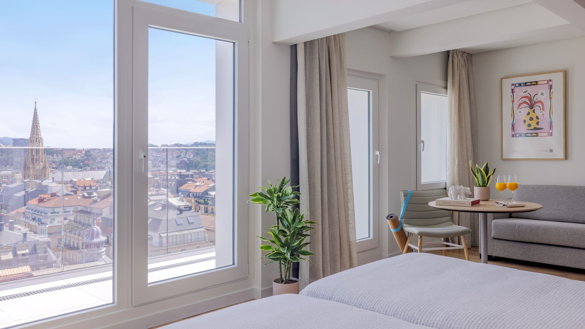 Habitación de hotel moderna con ventanales y vista urbana a la catedral.