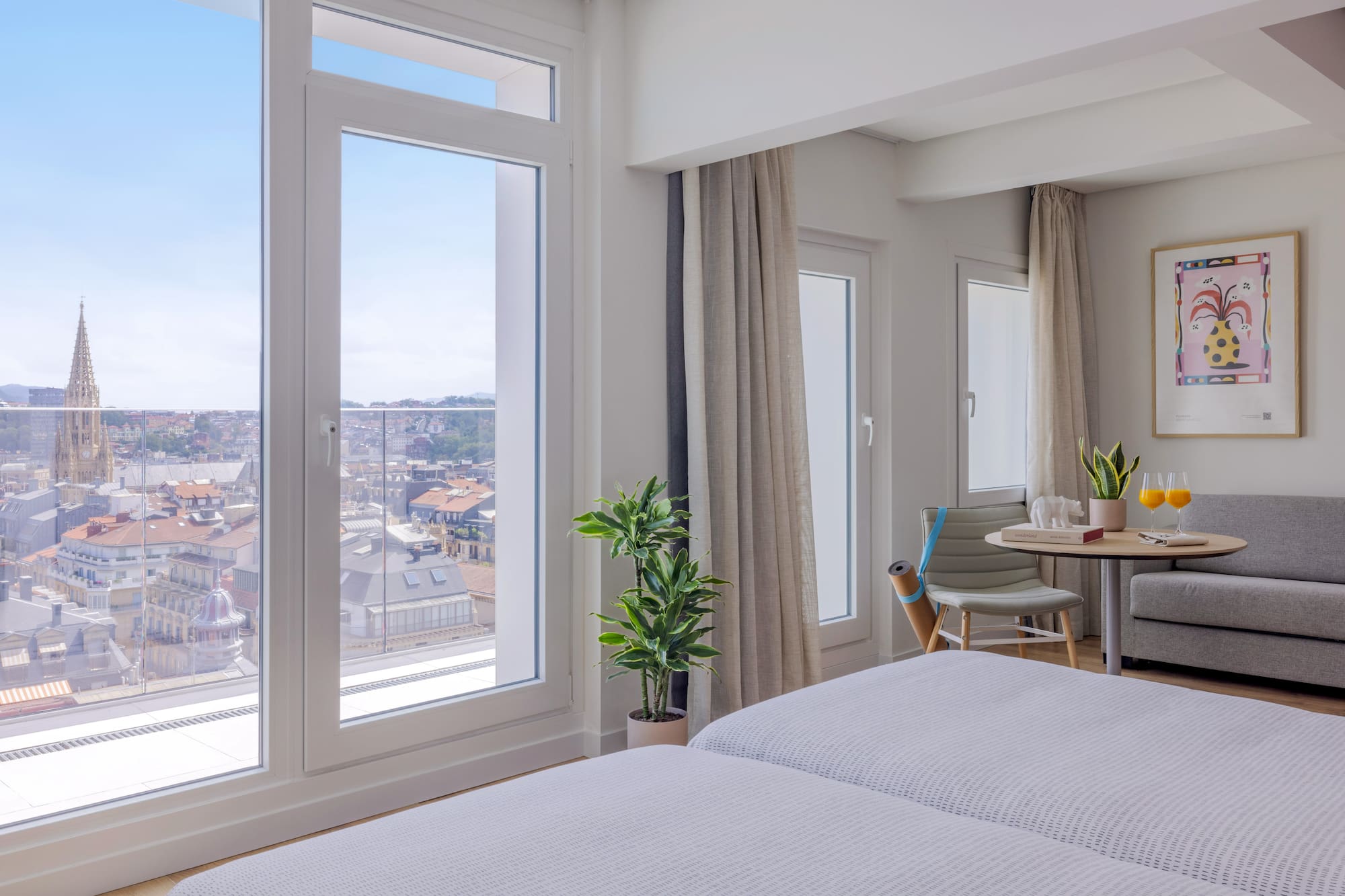 Habitación de hotel moderna con ventanales y vista urbana a la catedral.