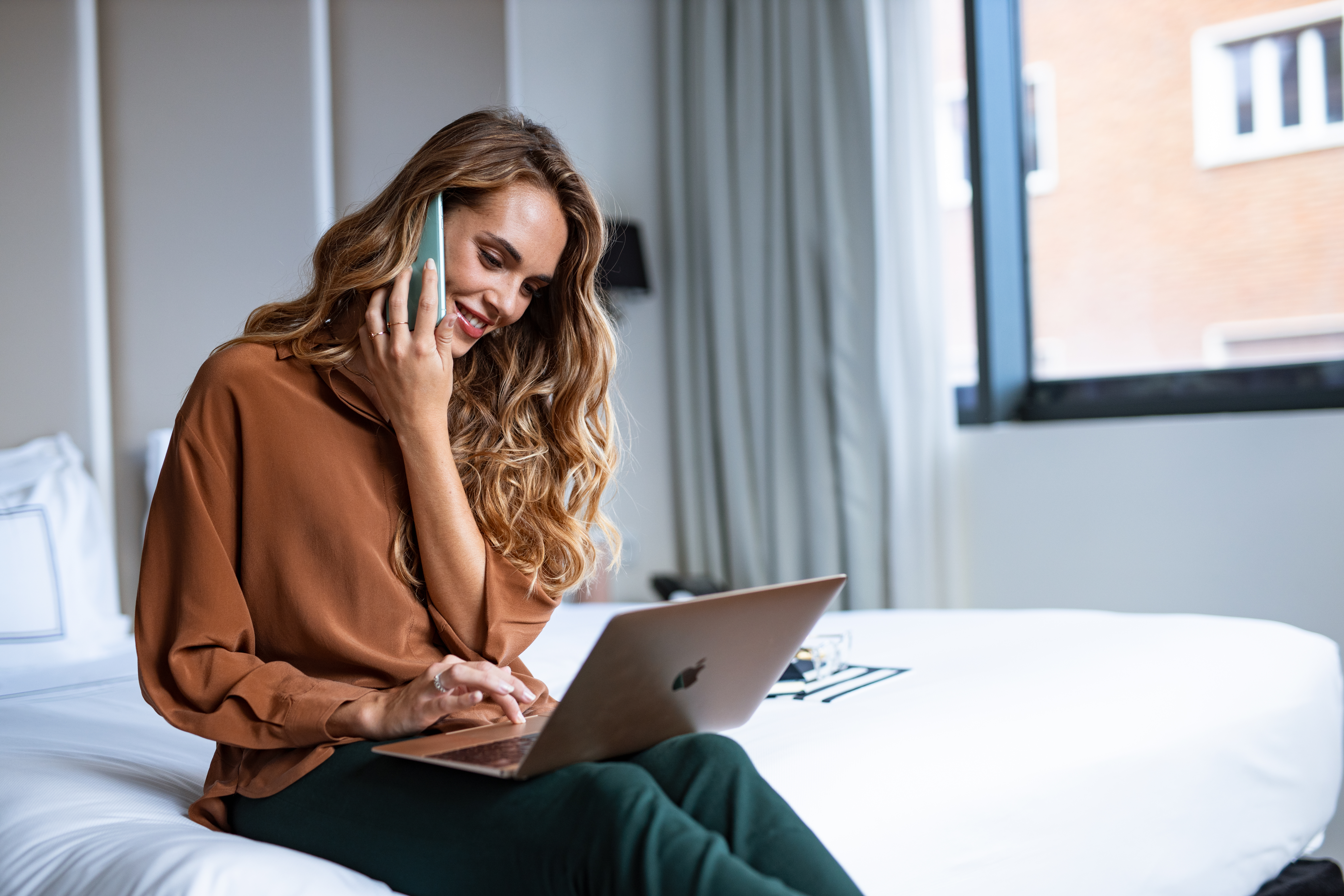 a woman sitting on a bed with a laptop and phone