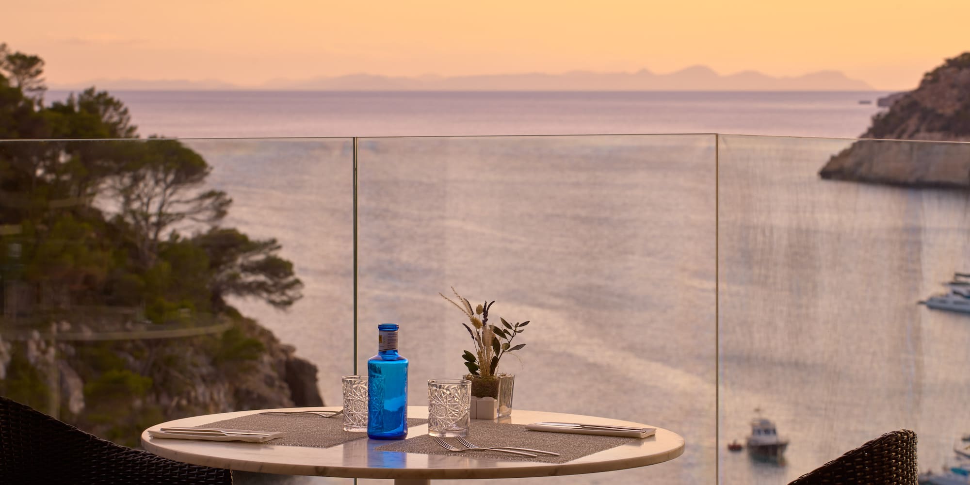a table with a glass bottle and glasses on it with a view of the ocean