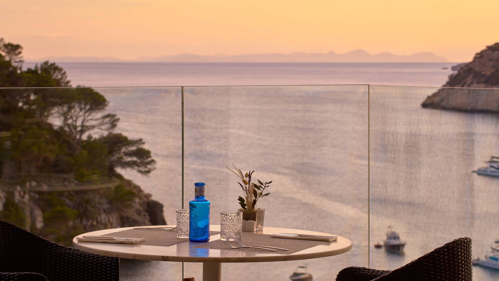 a table with a glass bottle and glasses on it with a view of the ocean