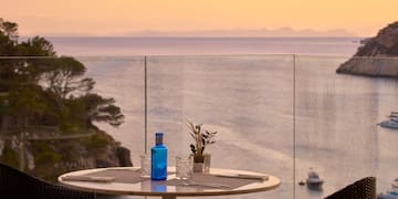a table with a glass bottle and glasses on it with a view of the ocean