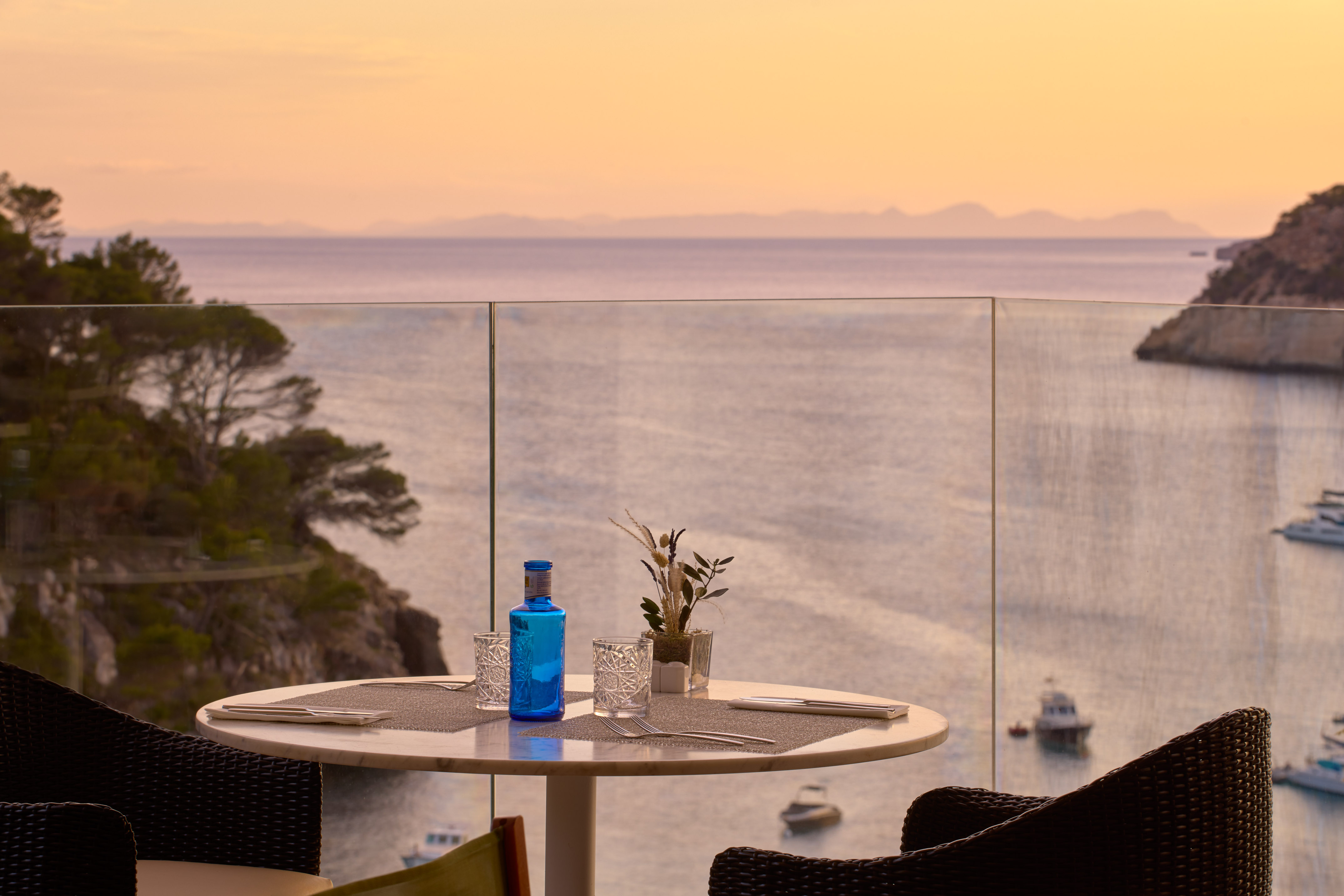 a table with a glass bottle and glasses on it with a view of the ocean