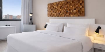 a bed with white sheets and pillows in a room with a lamp and a window