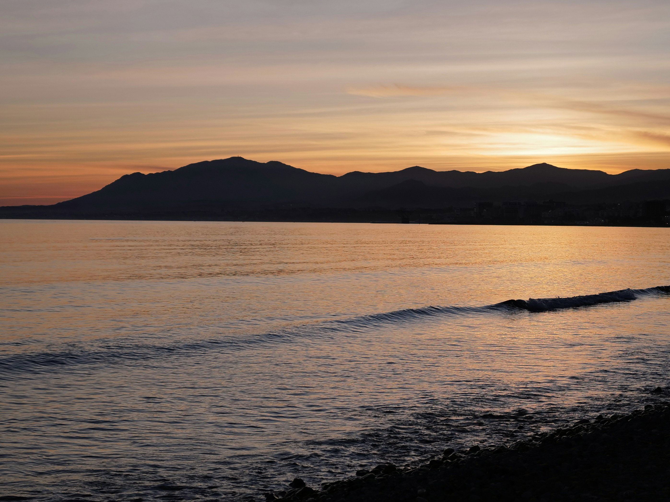 Golden sunset reflects on ocean waves, silhouetting coastal mountains.