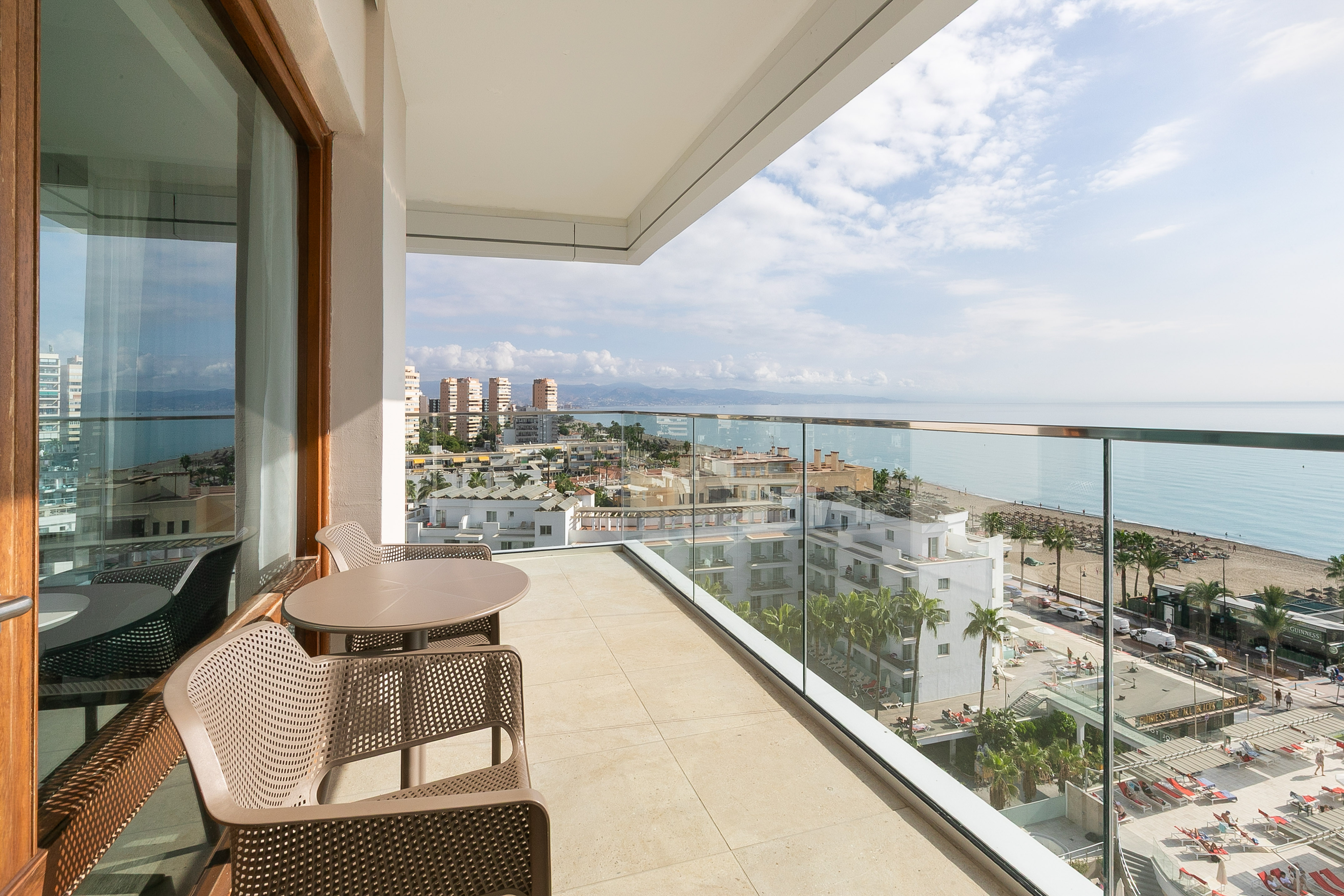 Modern hotel balcony with sea view, overlooking beach and coastal city.