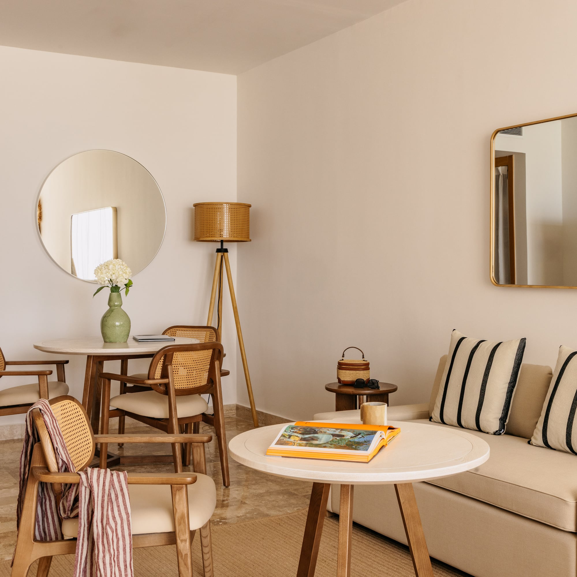 Contemporary hotel suite with neutral decor, rattan chairs, and sofa.