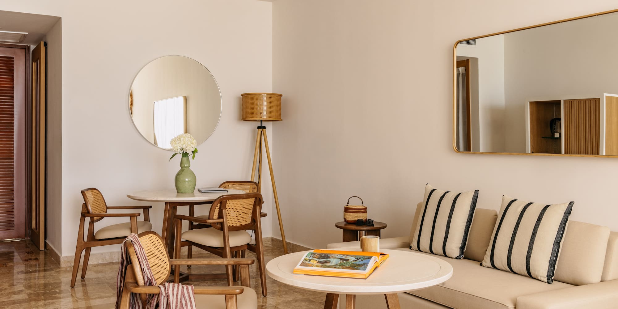 Contemporary hotel suite with neutral decor, rattan chairs, and sofa.