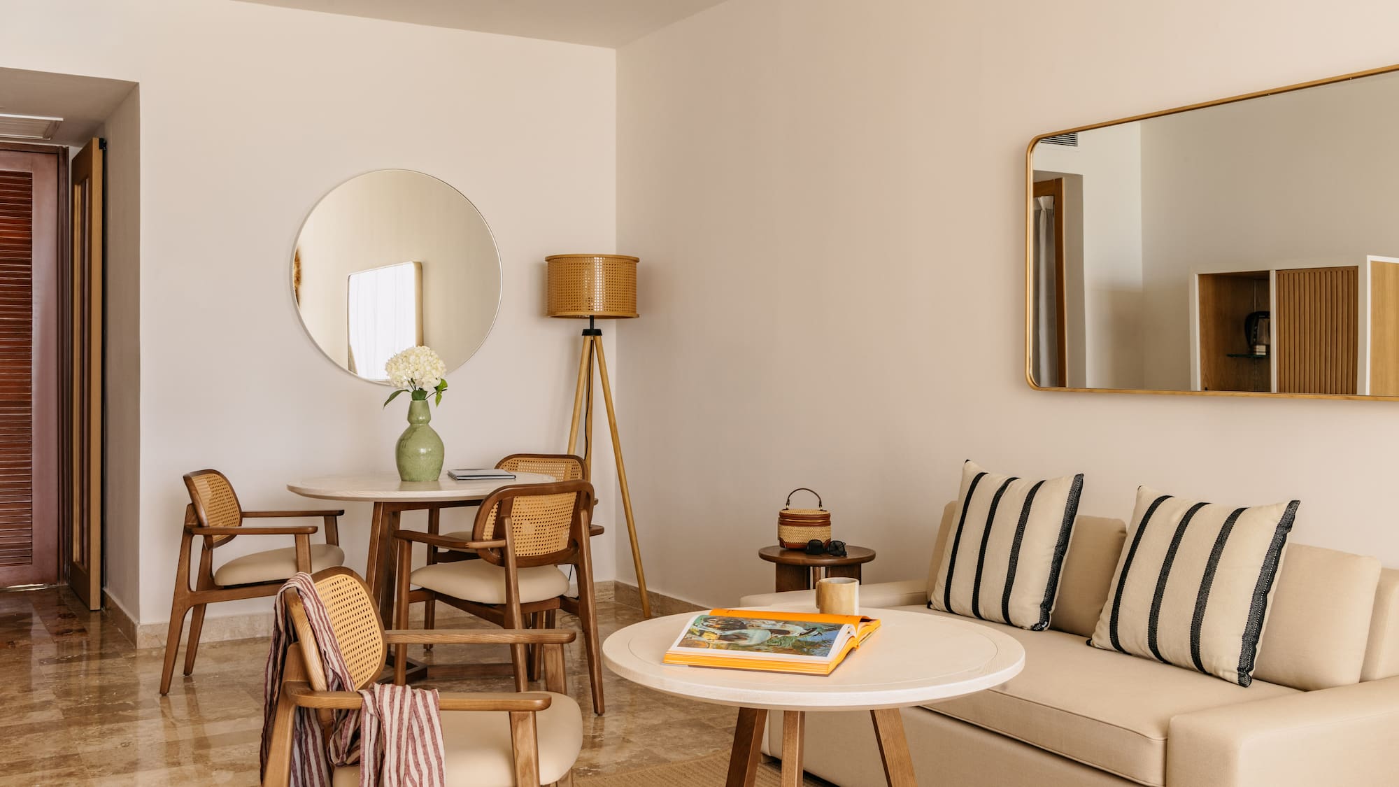 Contemporary hotel suite with neutral decor, rattan chairs, and sofa.