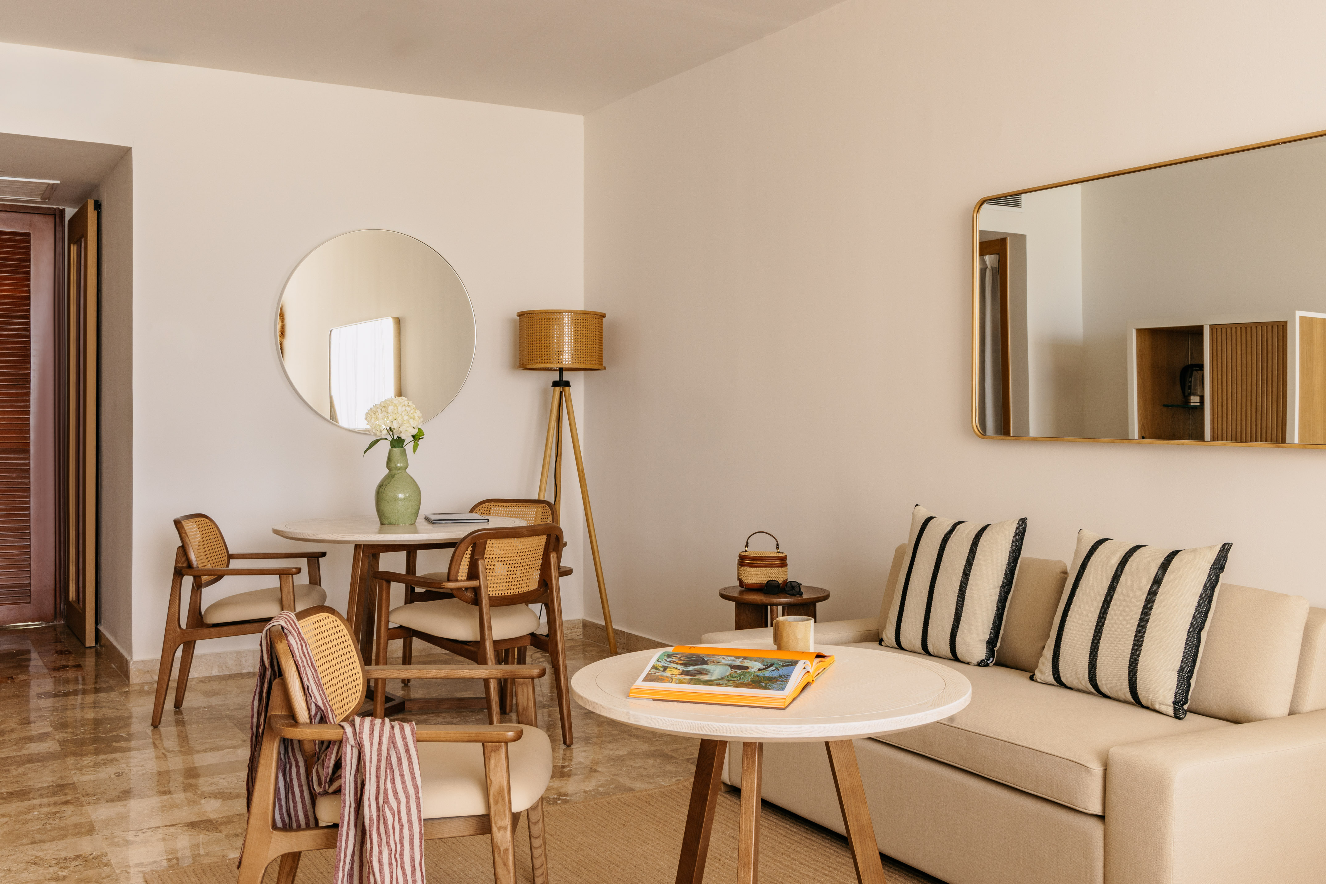 Contemporary hotel suite with neutral decor, rattan chairs, and sofa.