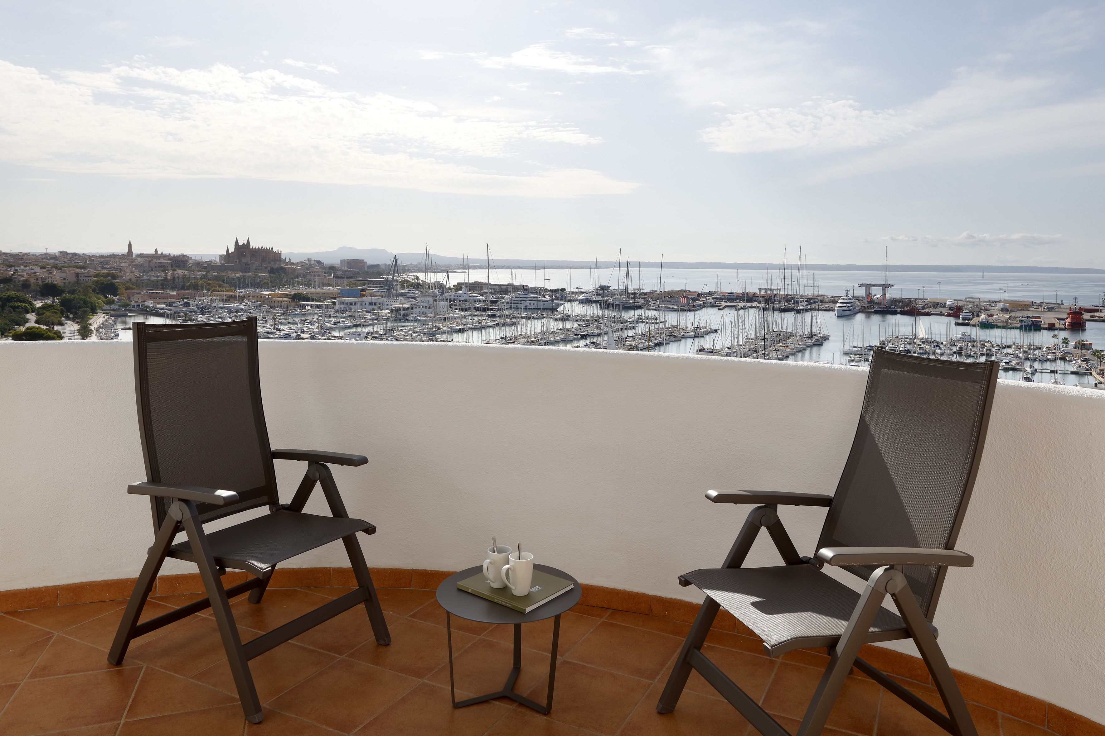Balcony view of Palma de Mallorca marina, city skyline, and two chairs on terrace.
