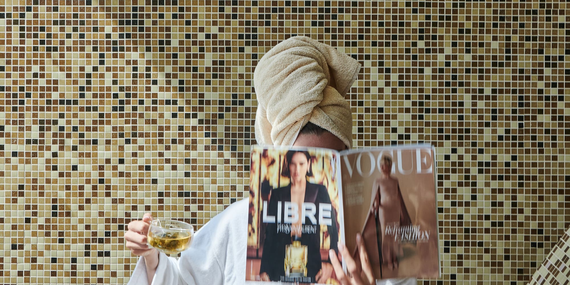 a woman in a white robe holding a magazine and a cup of tea
