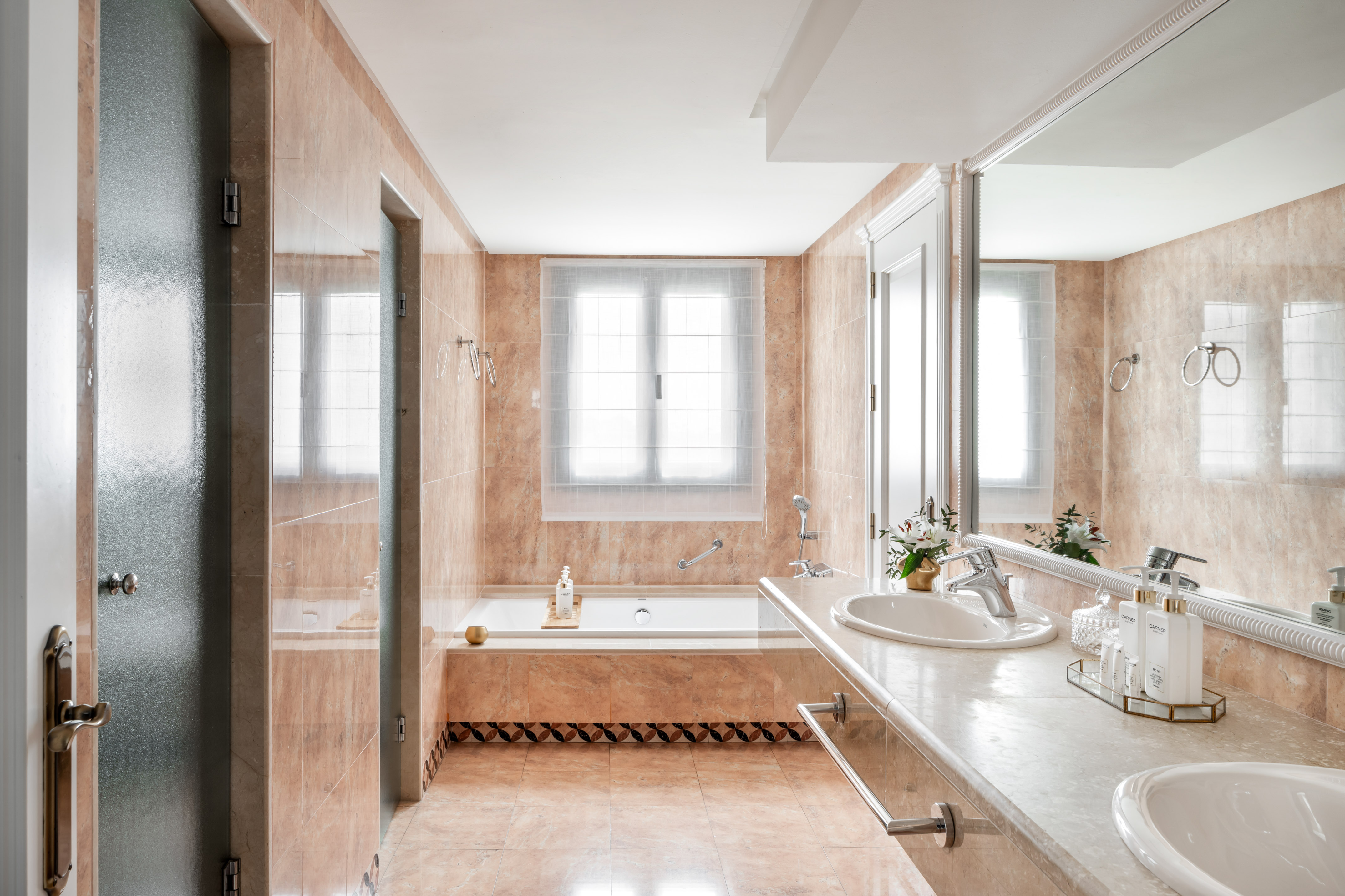 Light marble tiled bathroom with built-in tub, double vanity, and large mirror.