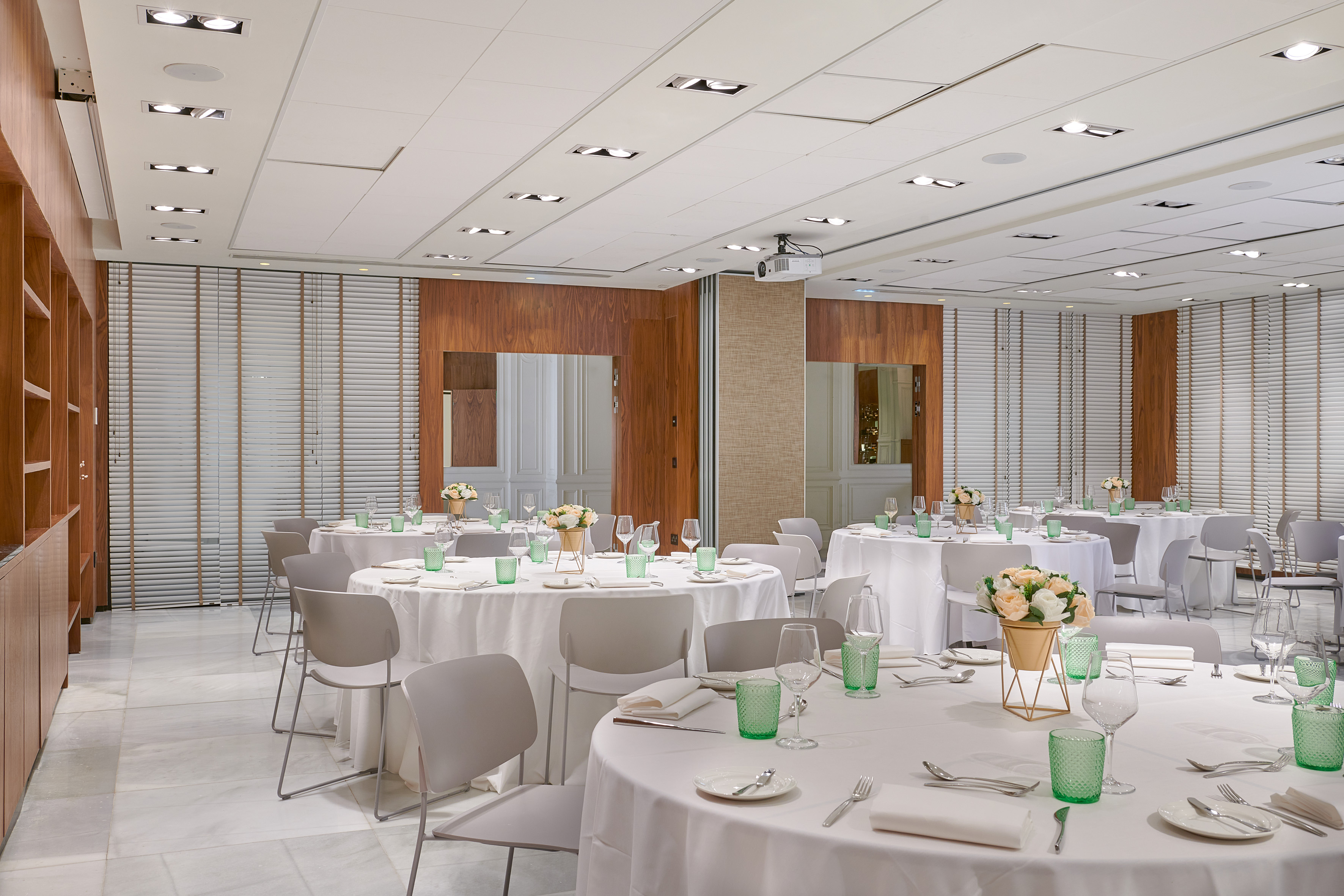Conference room with round tables, white linens, floral decor, projector.