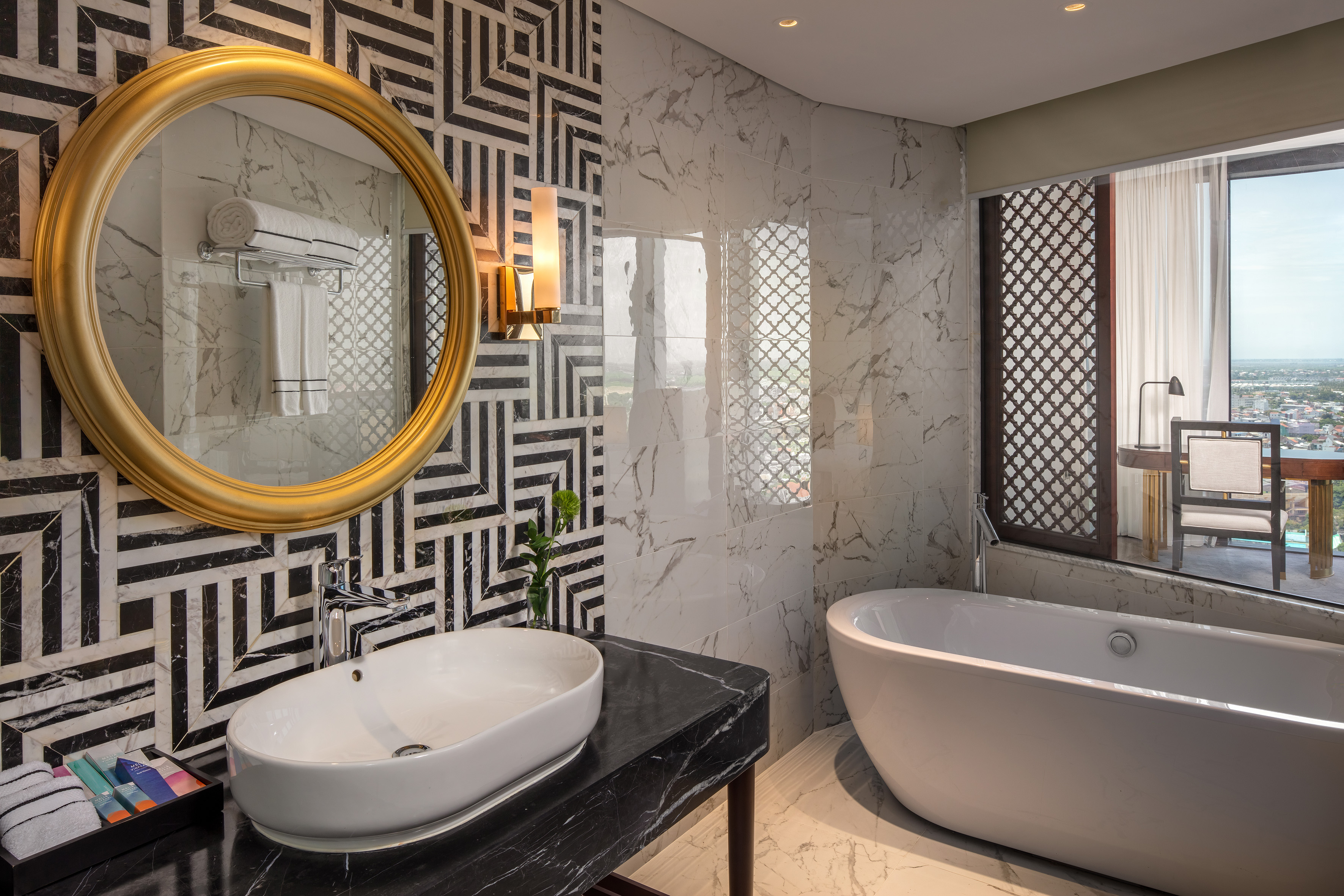 Luxury bathroom with geometric tiles, gold mirror, marble, freestanding tub.